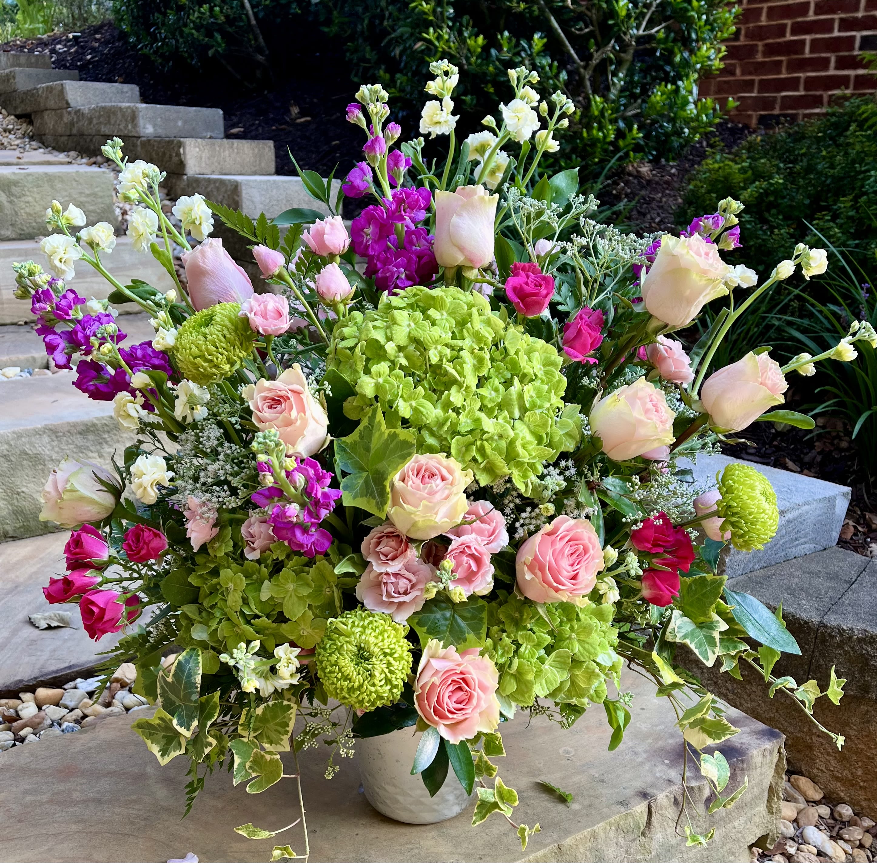 Romance Garden - Soft and elegant, this garden-inspired bouquet pairs delicate blush roses with vivid fuchsia blooms, vibrant green hydrangea, and textured accents of ivy and lime green poms. Overflowing with freshness and charm, it evokes the feeling of strolling through a blooming garden at the height of springtime romance.