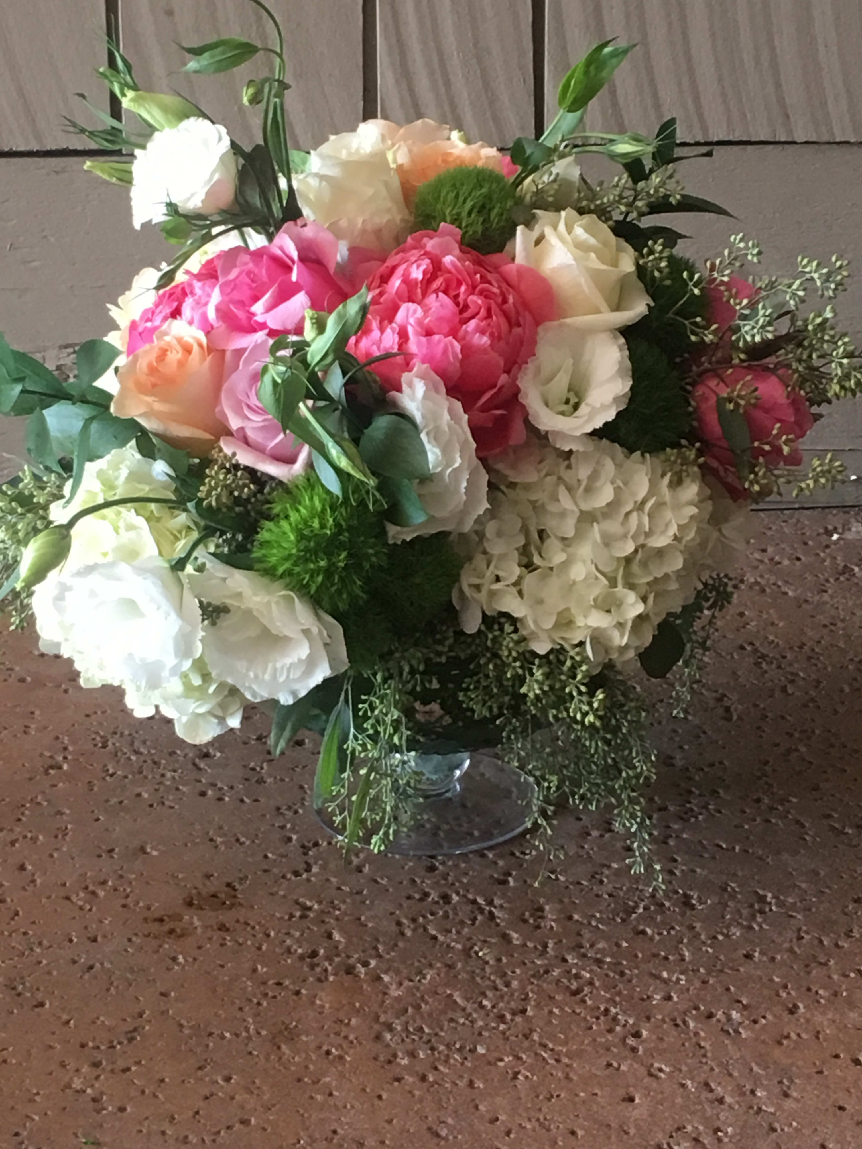 Pedestal Glass Vase Arrangement - Mixture of peach,baby pink, white roses, with peonies, hydrangeas, lisianthus, seed eucalyptus, green dianthus arranged in a beautiful glass pedestal round vase wrapped in banana leaves. 
