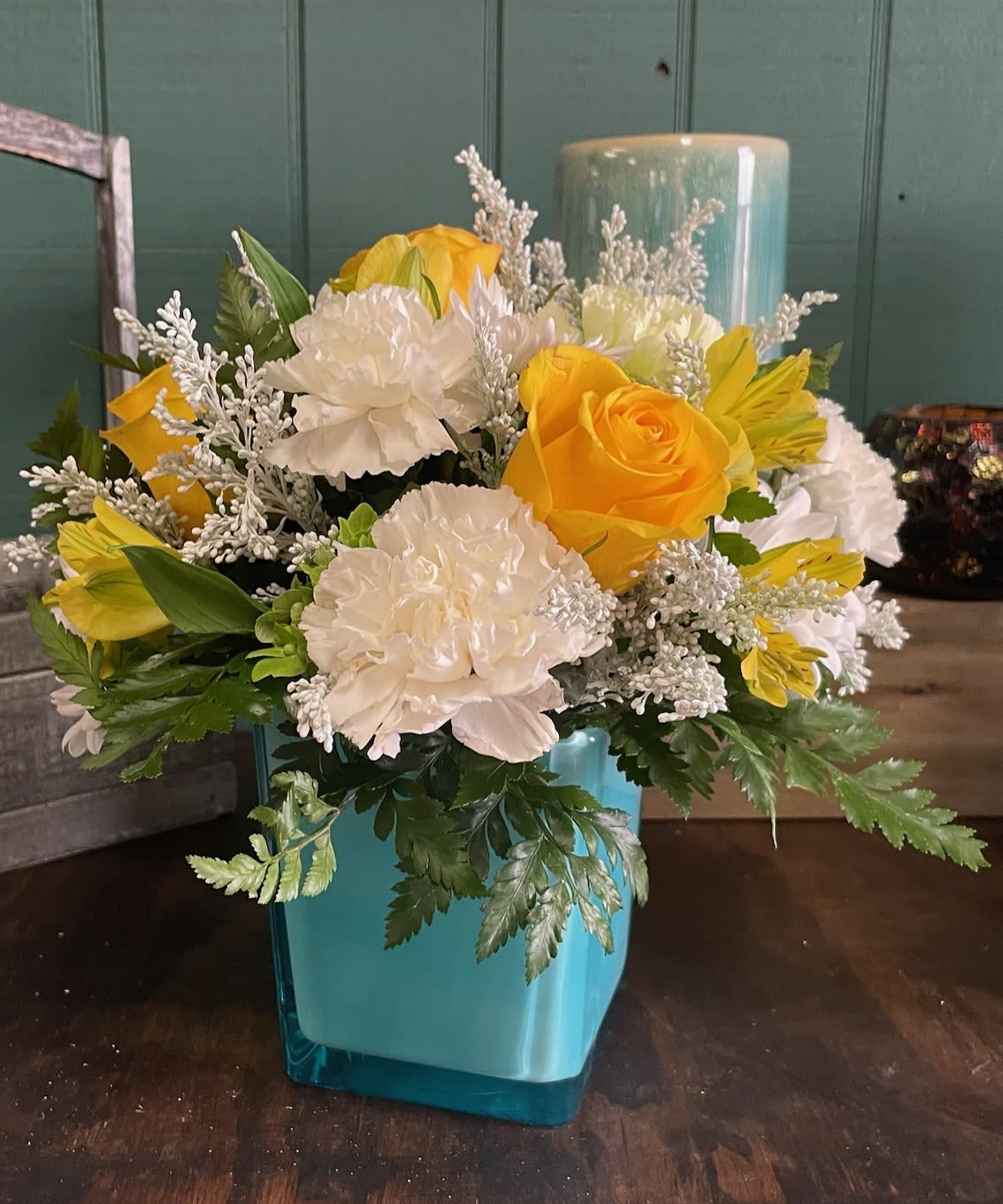 Sunshine Delight - Brighten any space with the cheerful glow of Sunshine Delight. This radiant arrangement features a harmonious blend of crisp white blooms and vibrant yellow flowers, evoking the warmth and joy of a sunny day. Accented with lush greens for added depth and texture, each bloom is thoughtfully arranged in a striking blue cube vase, creating a delightful contrast that’s both fresh and uplifting. Whether celebrating a special occasion or simply spreading happiness, Sunshine Delight is a perfect choice to bring a little sunshine to someone’s day!