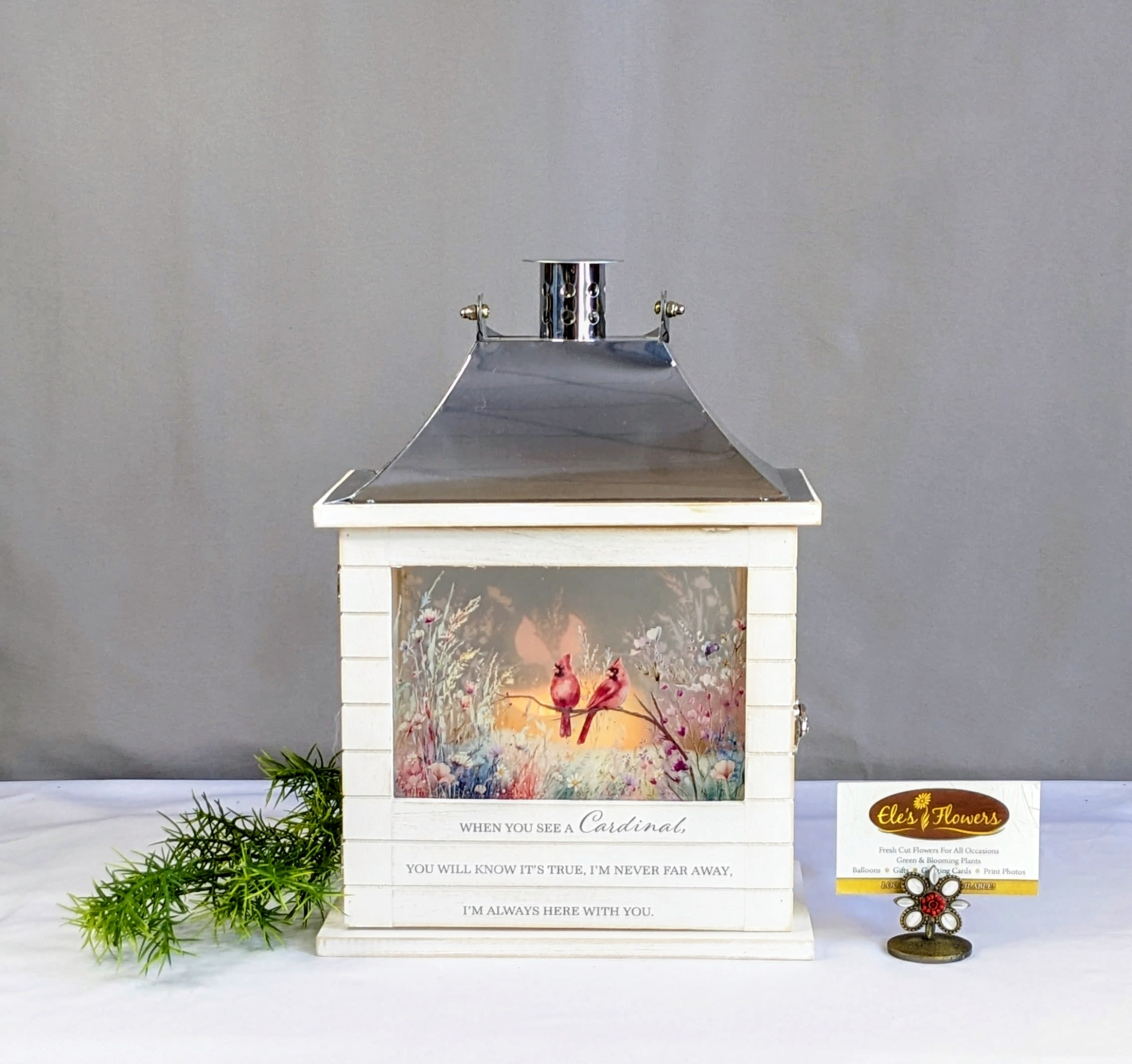Cardinal - Sympathy Lantern - A wonderful keepsake lantern to remember a loved one. This lantern is constructed of wood material with a decorative silver top and painted cardinals and wildflowers. The phrase "When you see a Cardinal, you will know it's true, I'm never far away, I'm always here with you." printed on the front. For indoor use only. Our Sympathy lanterns are powered by 3 AAA batteries (included). A flicker candle illuminates the lantern.  Approximate Dimensions: 14"H x 9"W 