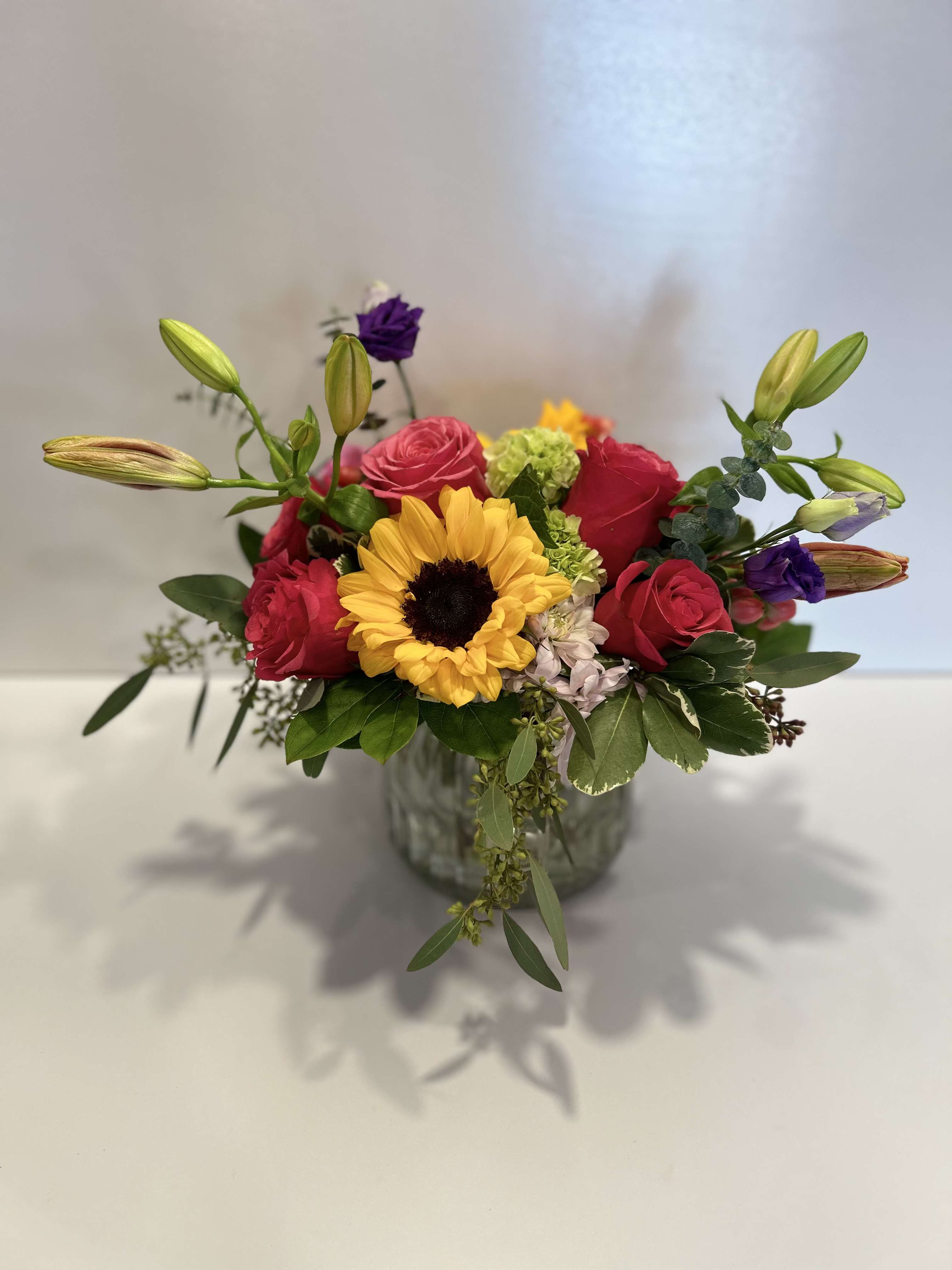 Little Bit of Sunshine - Sunflowers &amp; Roses - This vibrant and joyful arrangement captures the essence of sunshine with a mix of bold and soft blooms. The bouquet is designed to be a cheerful pick-me-up, ideal for brightening any space or occasion.  Care tips: Daily Maintenance +Display in a cool area: Place the bouquet in a cool, ventilated area away from direct sunlight, heat sources, and drafts. Avoid fruit: Keep the arrangement away from ripening fruit, which releases ethylene gas that causes flowers to wilt faster. +Remove old blooms: Promptly remove any flowers or leaves that start to wilt or yellow to prevent bacteria growth and keep the rest of the bouquet healthy.   Water and Stem Care +Clean vase: Always use a thoroughly cleaned vase to prevent the buildup of bacteria, which can clog the stems and stop water absorption. +Fresh, cool water: Use fresh, cool water and add the provided flower food packet to nourish the flowers and limit bacteria. +Change the water daily: Sunflowers are very thirsty and need fresh water often. Change the water every day, or at least every other day, and clean the vase each time. +Trim stems: Re-cut the stems diagonally by about an inch every time you change the water, using clean, sharp shears or a knife. This helps the stems absorb water efficiently. +Remove submerged foliage: Ensure no leaves sit below the waterline, as they will rot and contaminate the water. 