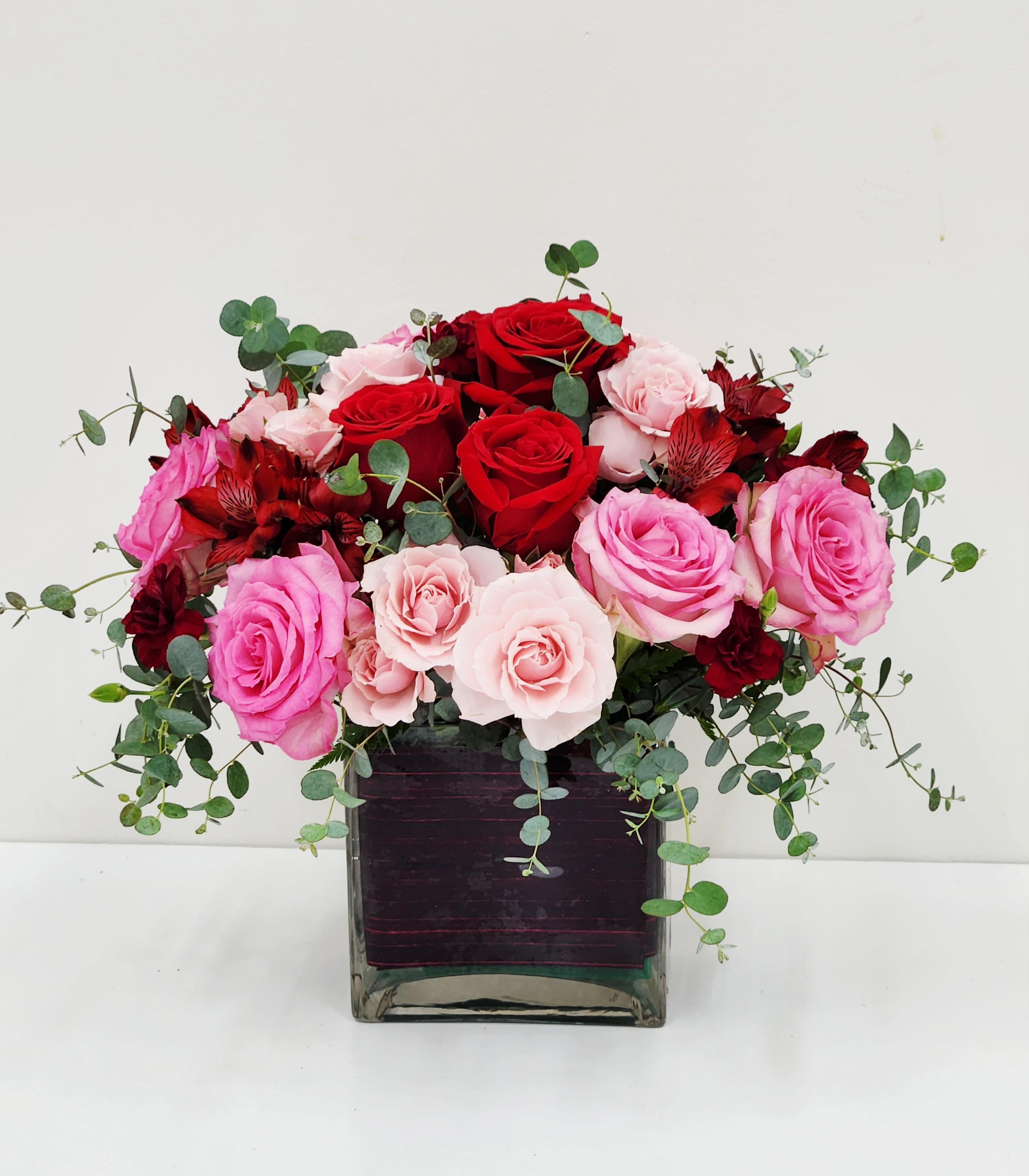 Heartbeat - Celebrate love and connection with Heartbeat, a stunning arrangement that captures emotion through color and form. Lush red, pink, and blush tones blend seamlessly, softened by the graceful movement of eucalyptus foliage. Nestled in a striking vase lined with deep crimson ti leaf, this composition balances romance with refined elegance—perfect for anniversaries, declarations, or moments that matter.