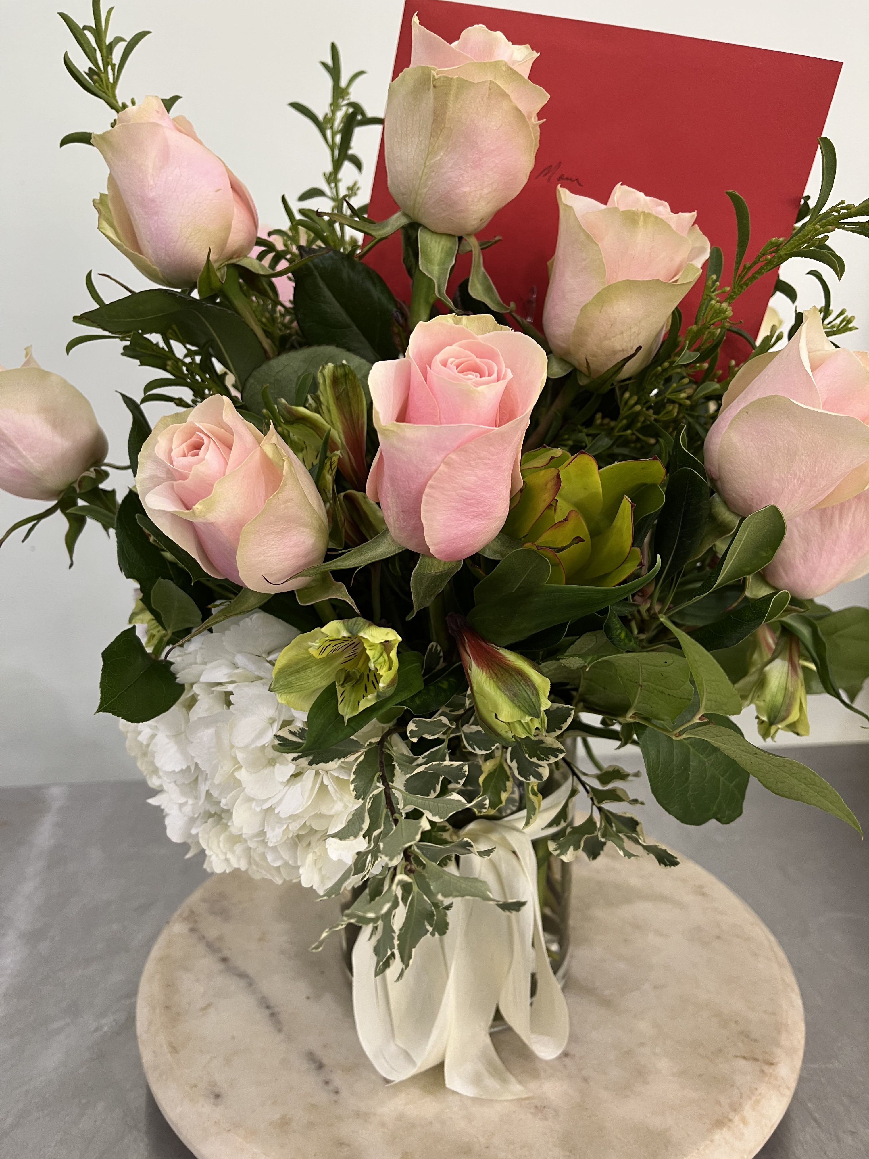 2026 Valentine's Day - Pink Roses!!! - Pink roses in a glass vase with additional flowers for a cottage garden look.  Flowers may include mums, tulips, and hyacinth.   For a traditional red rose arrangement with babies breath - please contact another local florist.