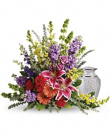 Shades Of Faith - A rainbow of reverence. This uplifting arrangement of lilies, roses and snapdragons is a beautiful reflection of a colorful life well lived. Pink stargazer lilies, lavender roses and yellow snapdragons are arranged with peach gerberas, hot pink carnations, lavender stock, bells of Ireland, purple larkspur, spiral eucalyptus and lemon leaf. Arrangement does not include urn.