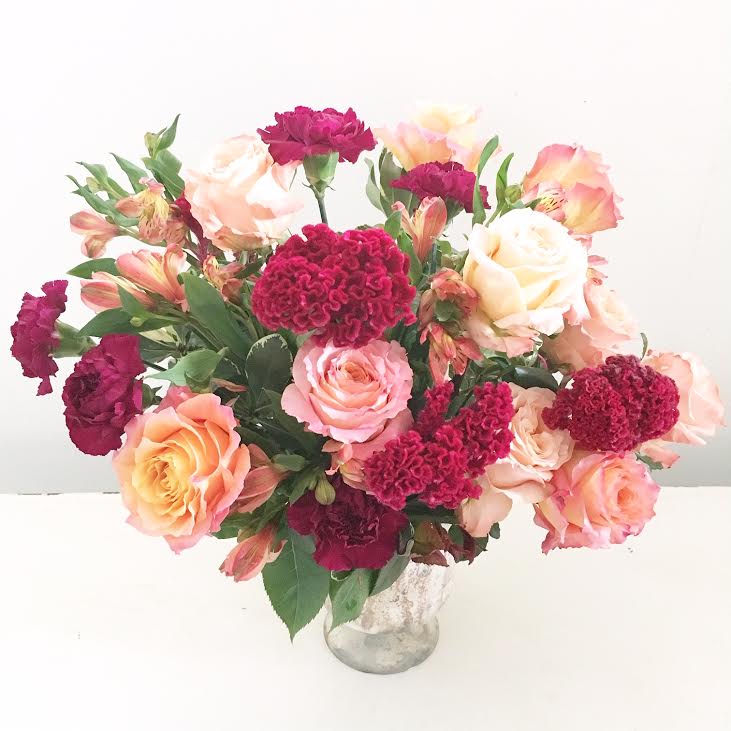 The Winona - A beautiful, full arrangement with ten gorgeous peach and sunset garden roses with a hint of burgundy antique French carnations and cockscomb celosia set in a glass pedestal vase.  *** Please NOTE: Do to the Covid-19 shutdowns, flower substitutions will most likely occur but we will strive to make them even more gorgeous than the photos :)