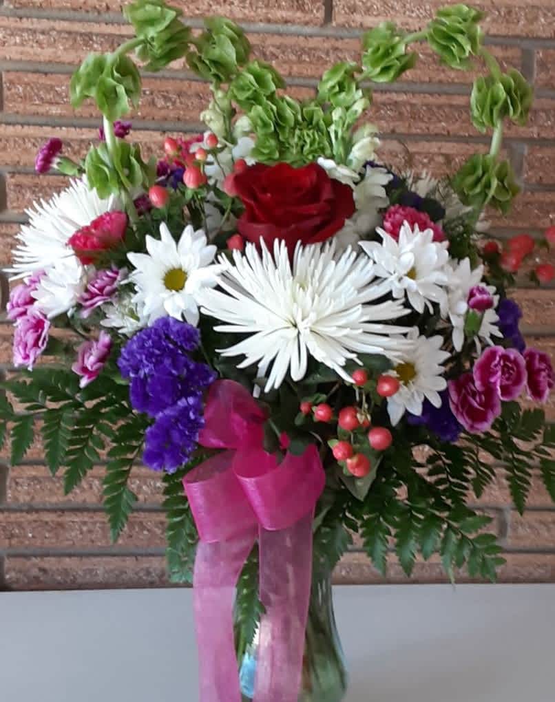 Cupid’s Pick - Make them blush with this romantic bouquet topped with lavish arches of greenery that form a heart. The flowers are selections of white, pink, red, and purple for a captivating Valentine’s Day inspired appearance. Just what Cupid ordered!  Our designer will hand-craft a one-of-a-kind arrangement, featuring flowers such as: roses, chrysanthemums, daisies, carnations, statice, hypericum berries, in shades of white, pink, red, and purple and paired in a vase with assorted greenery.