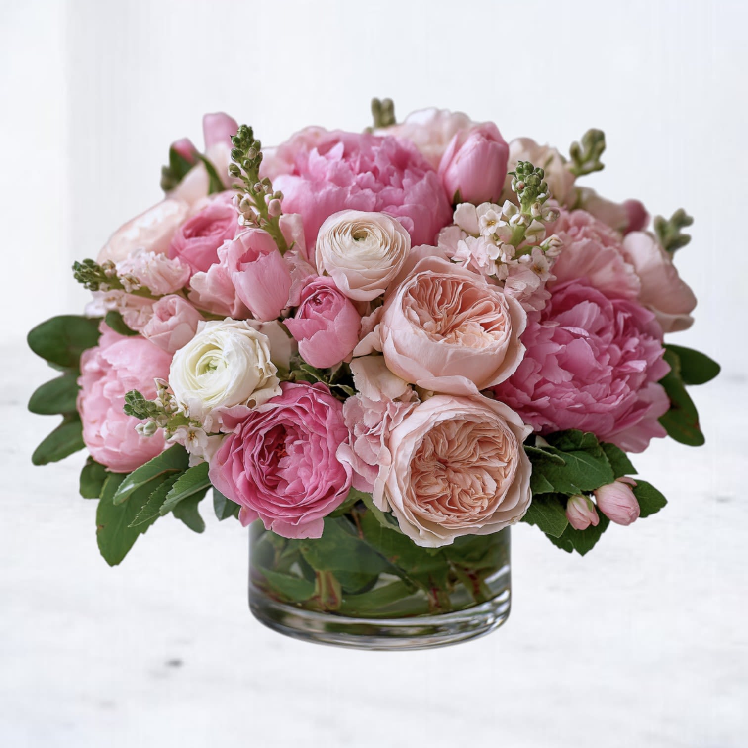 Elowen - Elowen is a graceful, garden-inspired arrangement designed with a refined, airy softness that feels both comforting and elevated. Featuring a lush blend of blush and pale pink blooms layered with creamy neutrals and fresh seasonal greenery, this design balances romance with restraint — never overly sweet, always intentional.  Styled in a clear glass cylinder vase, Elowen highlights natural textures, open petals, and gentle movement for an effortlessly elegant presentation. Its versatile palette makes it a thoughtful choice for birthdays, celebrations, thank-yous, sympathy gestures, or simply sending something beautiful “just because.”  Each arrangement is handcrafted with premium seasonal flowers and designed to feel full, fresh, and naturally abundant from every angle.