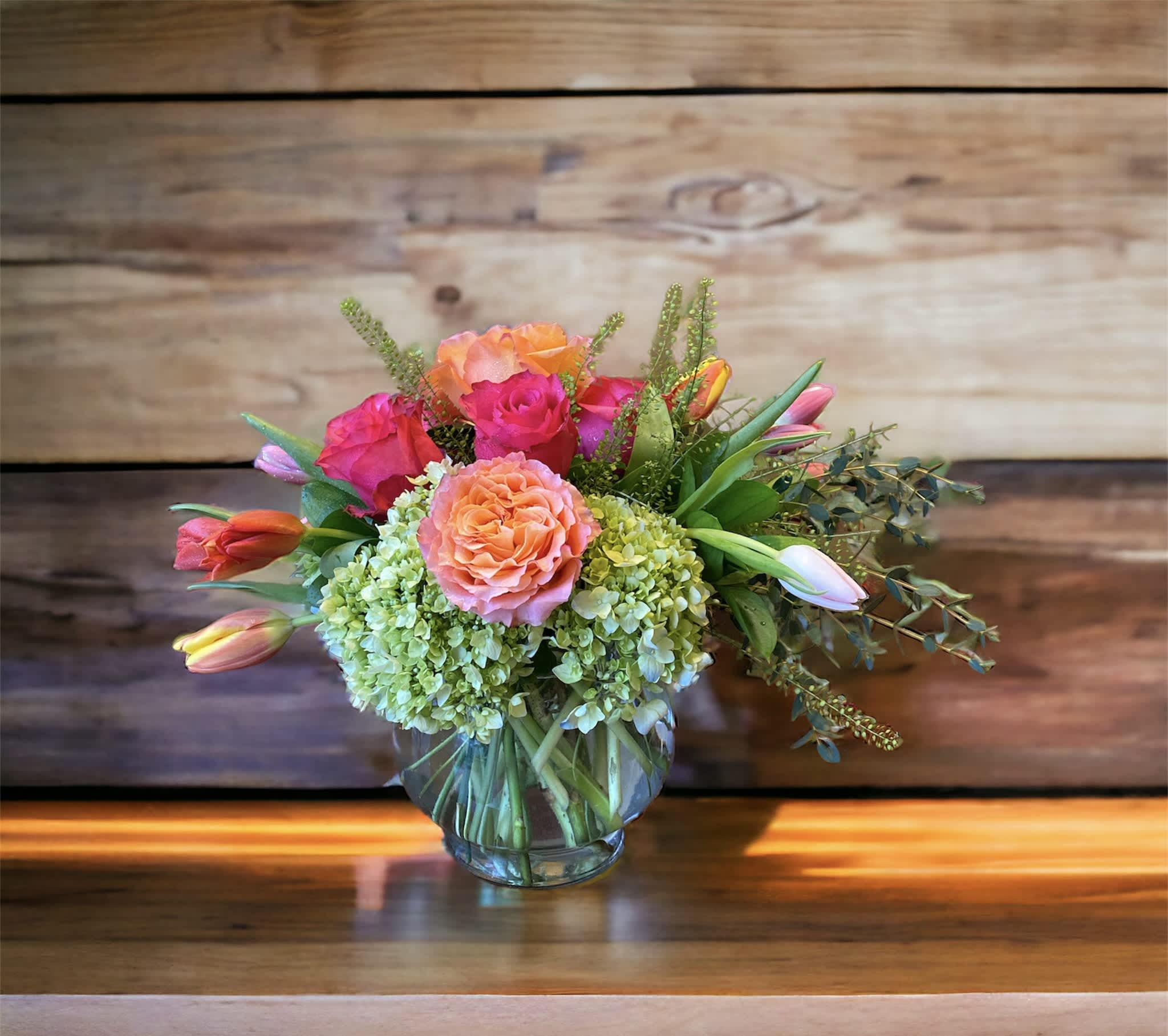 Blush Life Bouquet - Go ahead, make them blush! This luxurious bouquet of roses, tulip and hydrangea in fresh shades of peach and green is sure to put some cheerful color in their cheeks!  This sweet arrangement features green hydrangea, hot pink roses, orange roses, pink and orange tulips, seeded eucalyptus, parvifolia eucalyptus, and lemon leaf. Delivered in a glass gathering vase.
