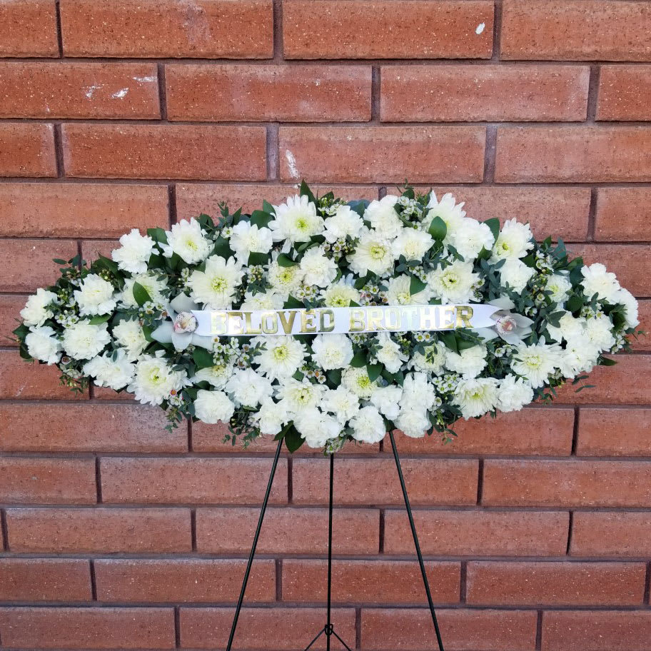 Surfboard Funeral Floral Tribute Standing Spray - Express your deepest sympathies to friends and family members with a beautiful surfboard-shaped arrangement, crafted by House of Stemms. Featured flowers include cymbidium orchid blooms, miniature chrysanthemums, carnations, waxflower and eucalyptus.  Our exclusive Surfboard Funeral Floral Tribute Standing Spray is appropriate for wakes, funerals, and memorial services. The flowers measure approximately 36in (W) x 16in (H), for a total of approximately 60 inches (H) when displayed on the easel stand. Deluxe version includes a banner as pictured.  Please Note: This is a special order floral arrangement. Surfboard shape is cut out of styrofoam, and flowers / greens are individually glued to the board. We highly recommend to schedule a pickup or delivery on the day of service to guarantee the freshness of this floral composition.  Place your order online and allow at least 2-3 business days for order processing. Please give us a call at 619-237-8842 for color and flower options.