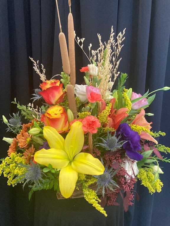 Golden Lily Harvest - Bring the beauty of a vibrant autumn meadow indoors with this stunning floral arrangement. Bursting with color and texture, it features bright yellow lilies, orange roses, deep purple blooms, and rustic cattails surrounded by lush greenery and seasonal accents. Perfect for celebrating fall, expressing gratitude, or adding a cheerful pop of color to any space.