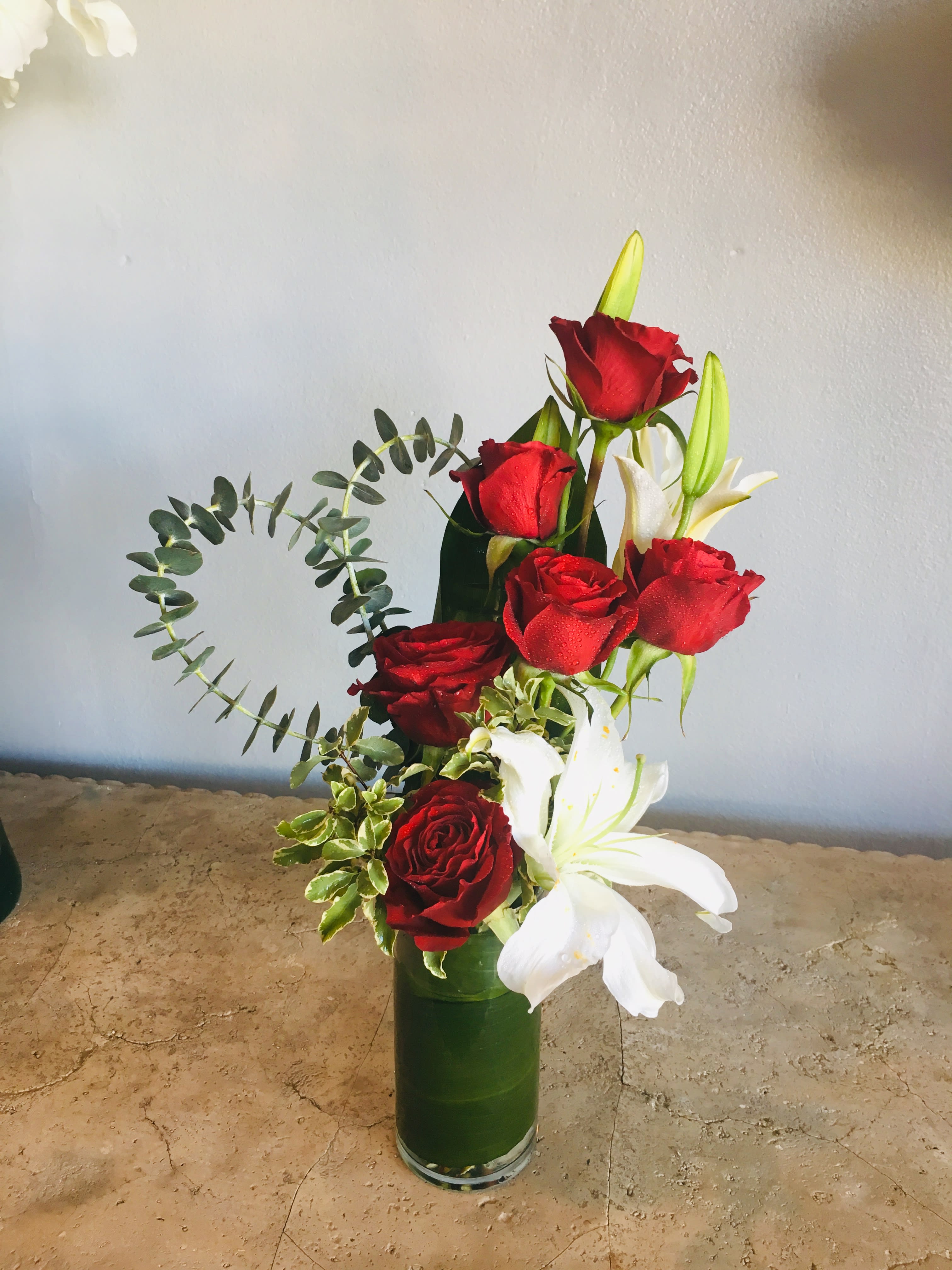 Heart of Hearts - A beautiful romantic gift of red roses, white lilies accented with eucalyptus branches in a green leaf wrap glass cylinder. Make for an unforgettable Occasion. Available for pickup or delivery in West Palm Beach, Palm Beach, Lake Worth, Palm Beach Gardens and surrounding areas.