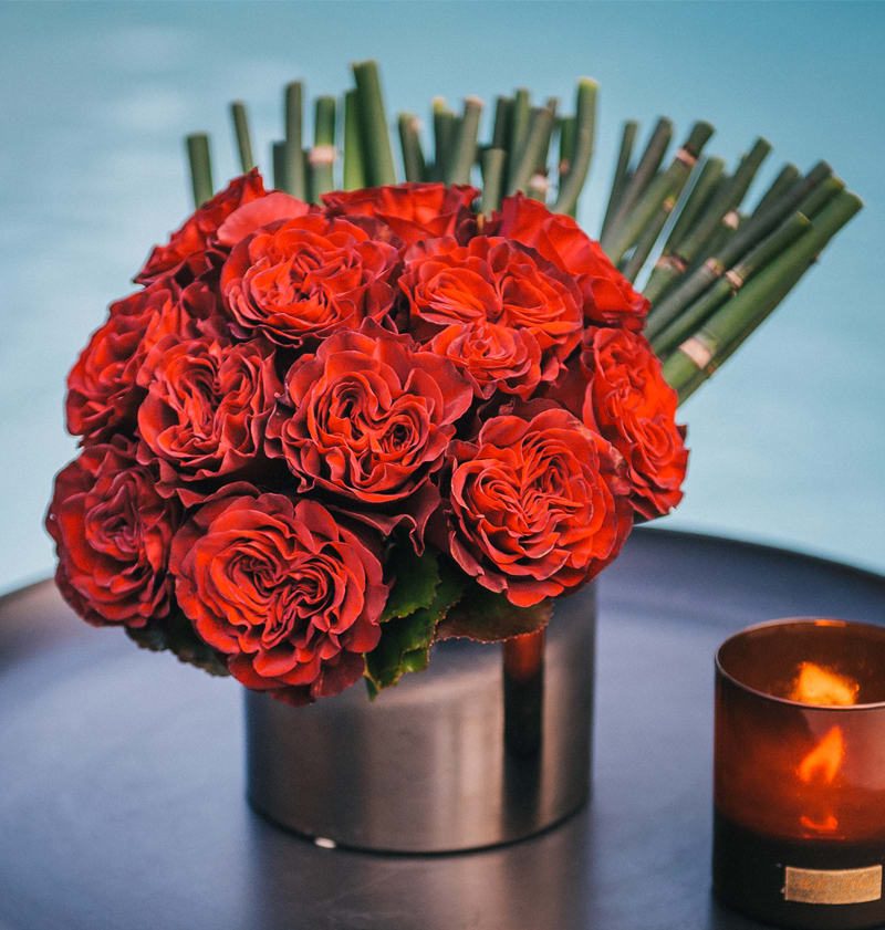 Delight - A silver cylinder featuring a tight grouping of ruffled red roses, hand-tied and accented with horsetail. 