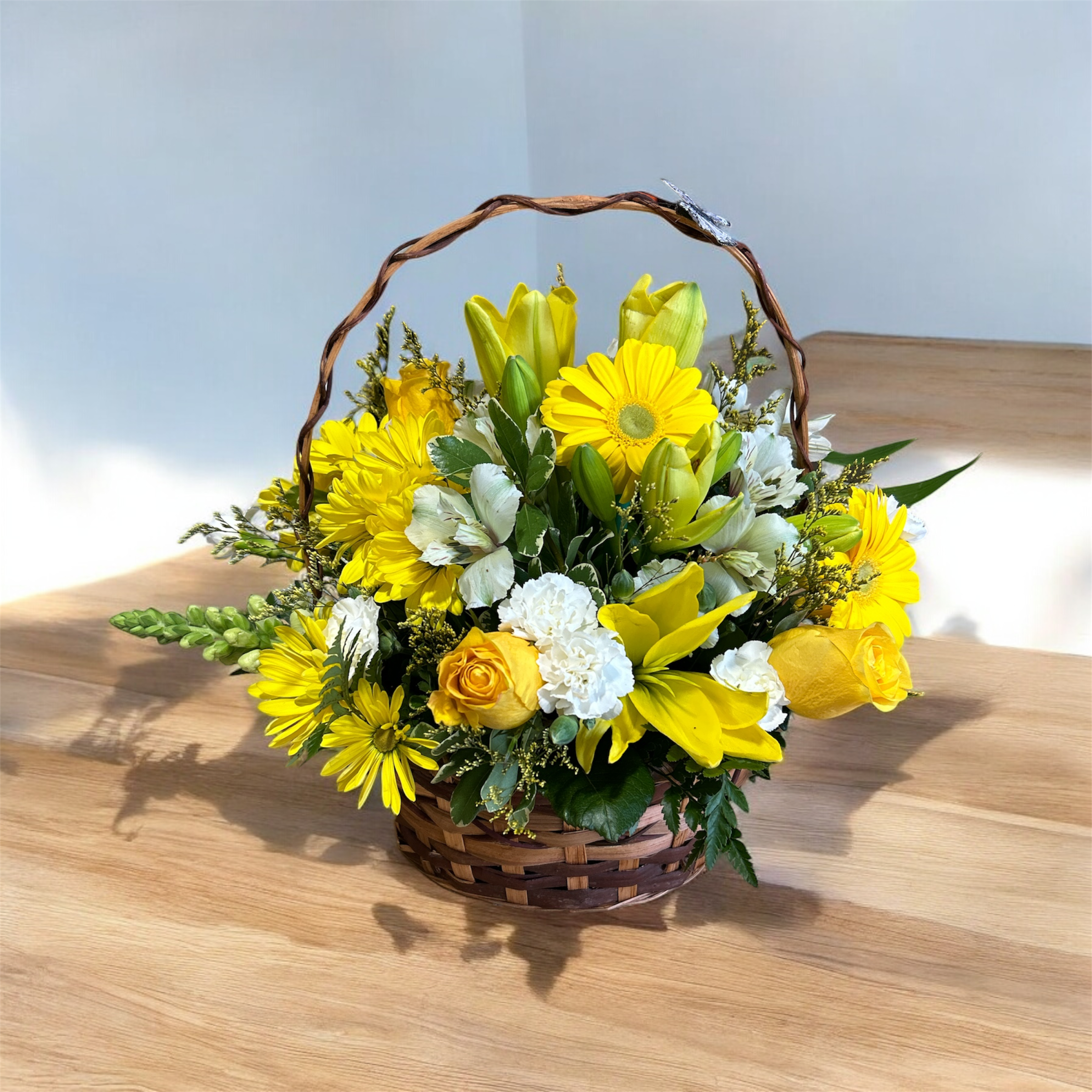 Sunlit Blessings Basket - Bright and uplifting, this brown basket is filled with a cheerful mix of blooms. Golden yellow lilies, gerberas, and daisies shine with warmth, while white alstroemerias, carnations, and snapdragons add a soft, graceful touch. A beautiful arrangement that brings comfort, hope, and light to any occasion.