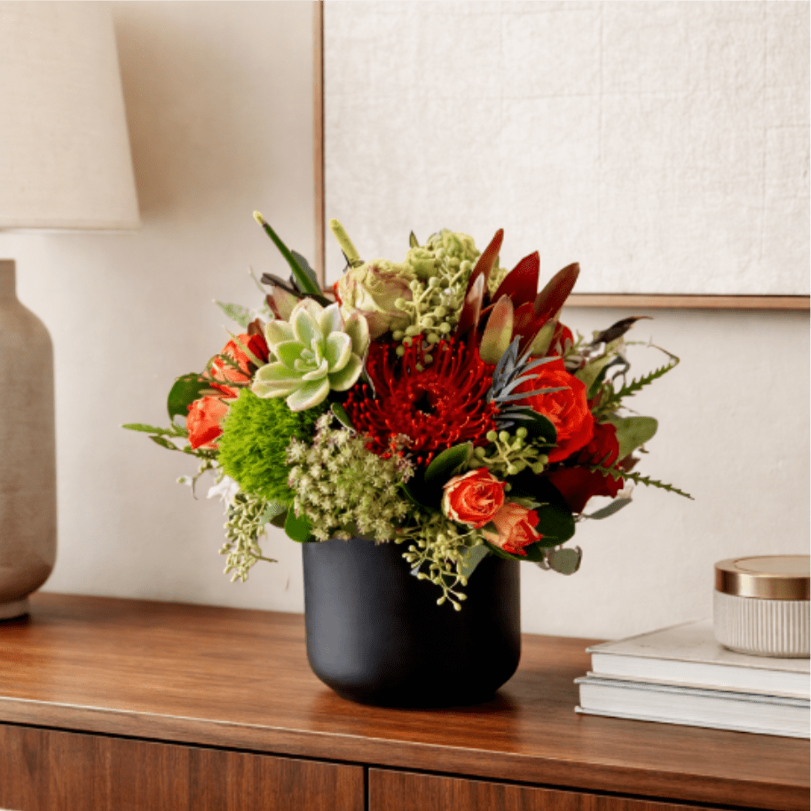 Maya Arrangement by My Blooming Business - Maya Arrangement by My Blooming Business Bold. Vibrant. Unforgettable. The Maya Arrangement is a stunning floral display designed to impress. Presented in a sleek matte black vase, this luxurious arrangement features striking orange protea, rich red and orange roses, lush green hydrangeas, and an assortment of textured greenery for depth and dimension. Perfect for modern spaces or as a statement gift, Maya brings warmth, sophistication, and a touch of the exotic to any occasion.  Ideal for celebrations, anniversaries, corporate gifting, or elegant home décor. Same-day flower delivery available in Los Angeles and surrounding areas.