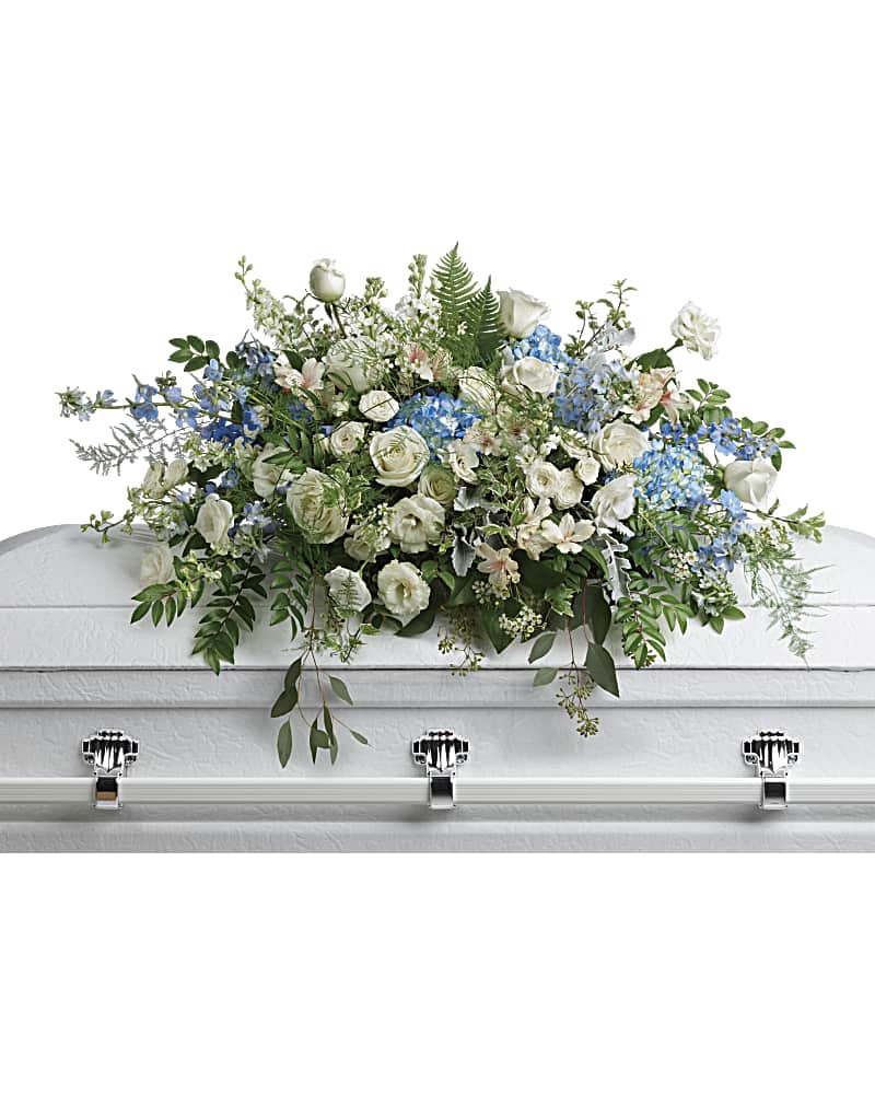 Tender Remembrance Casket Spray - As soft and delicate as a tender remembrance, this stunning spray of sky blue hydrangea and pure white roses brings a fresh, natural beauty to the casket. This stunning spray includes blue hydrangea, white roses, white spray roses, white alstroemeria, white lisianthus, blue delphinium, white larkspur, white stock, white waxflower, dusty miller, huckleberry, asparagus plumosus, pitta negra, lily grass, dagger fern, and lemon leaf.