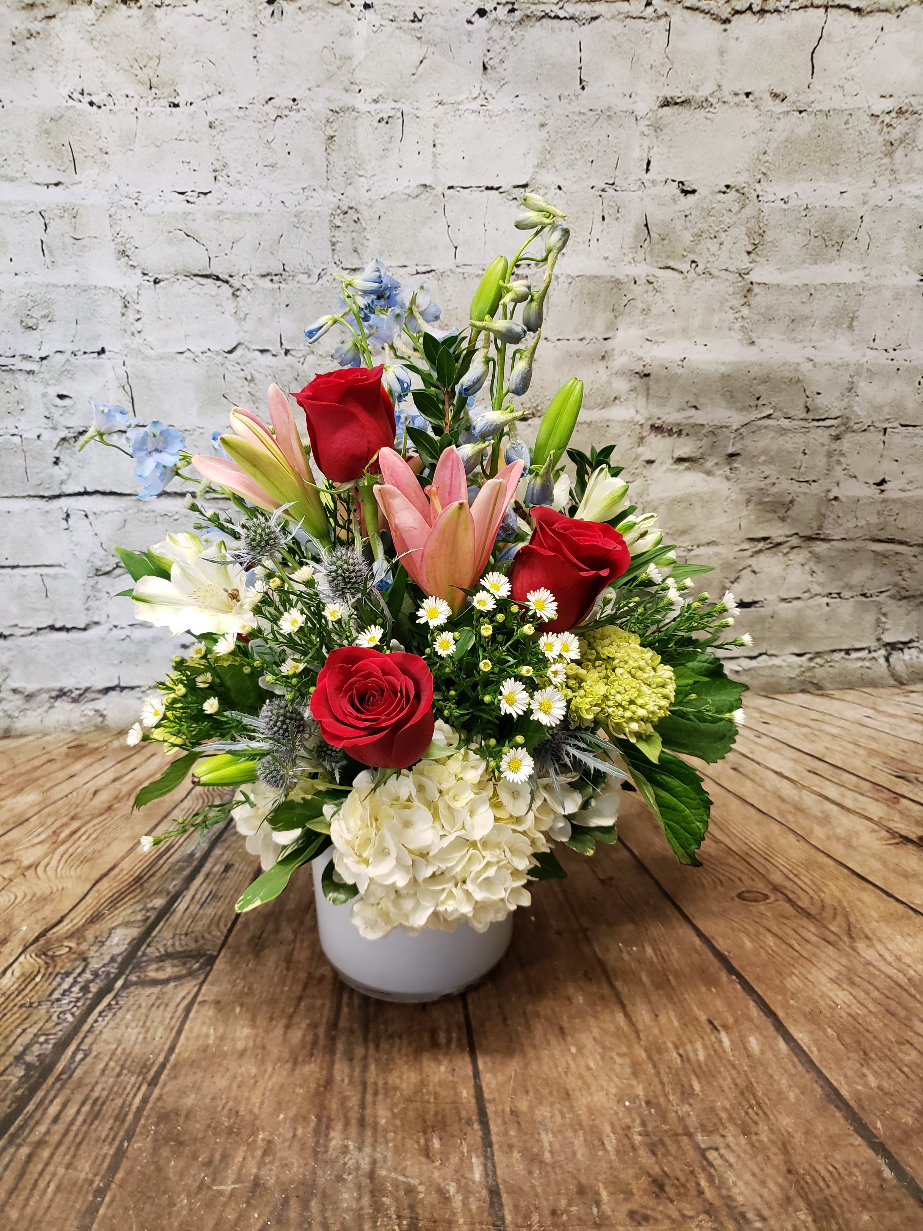Meant To Be - A sleek white cylinder vase holds a pretty display of white and green hydrangea, blue delphinium, pink lilies and romantic red roses.  