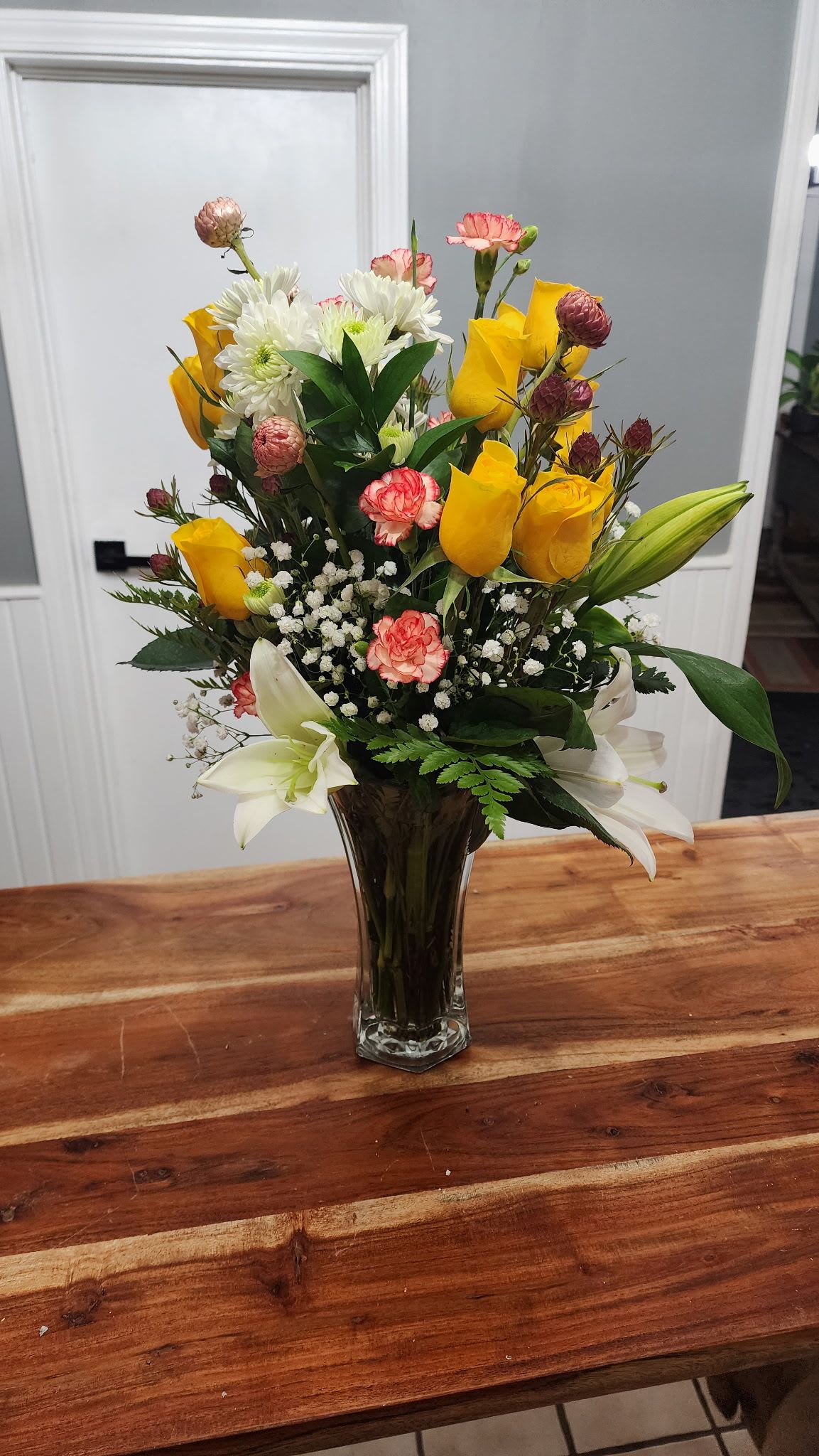 Fun in the sun  - Yellow roses, white daises and lillies, and two-tone mini carnations with greenery in a vase.
