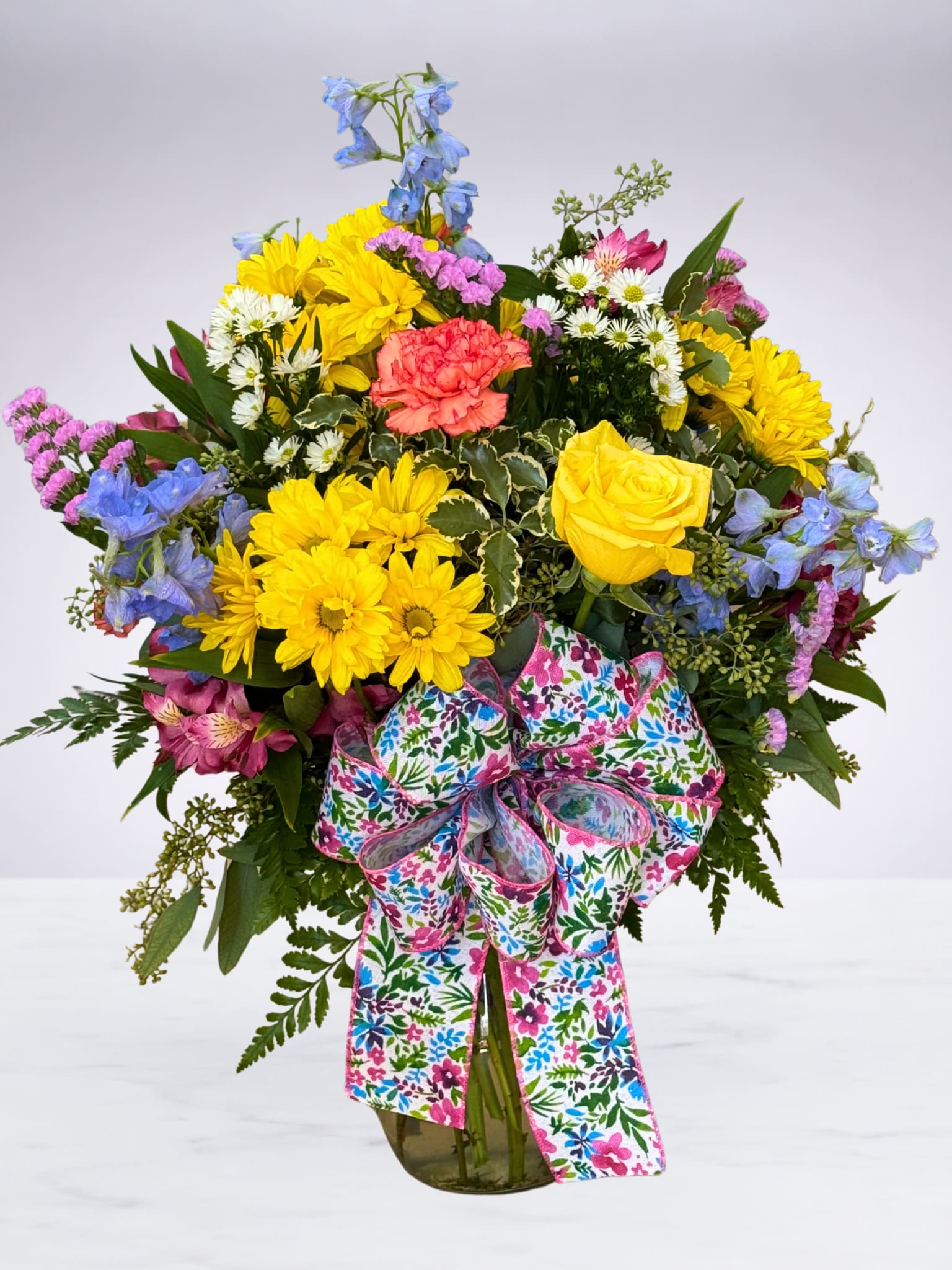 Spring Meadow Blooms - A cheerful mix of colorful seasonal flowers designed to capture the fresh beauty of spring. Accented with lush greenery and finished with a festive bow, this bright bouquet is perfect for celebrating any occasion. Flower varieties and colors may vary, making each arrangement uniquely beautiful.