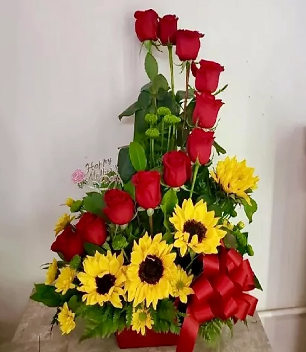 VDay 7 - This beautiful arrangement comes with 12 roses medium stem 60 cm along with 4 sunflowers and yellow daises and greenery in a square vase with red bow.  DISCLAIMER  For green and blooming plants, similar plants may be substituted of equal or greater value. For flowers, we will make every attempt to match the flower type / color but may substitute with another color or type of flower. If the container/ vase shown online is not available, a similar container/ vase will be used. Bears or other gift items may be substituted as well.  Want to check on availability? If it makes you feel more comfortable about the purchase, then we encourage you to call or email us to check on the latest availability of certain products. We would be glad to give you the most current, up-to-date status on our inventory.