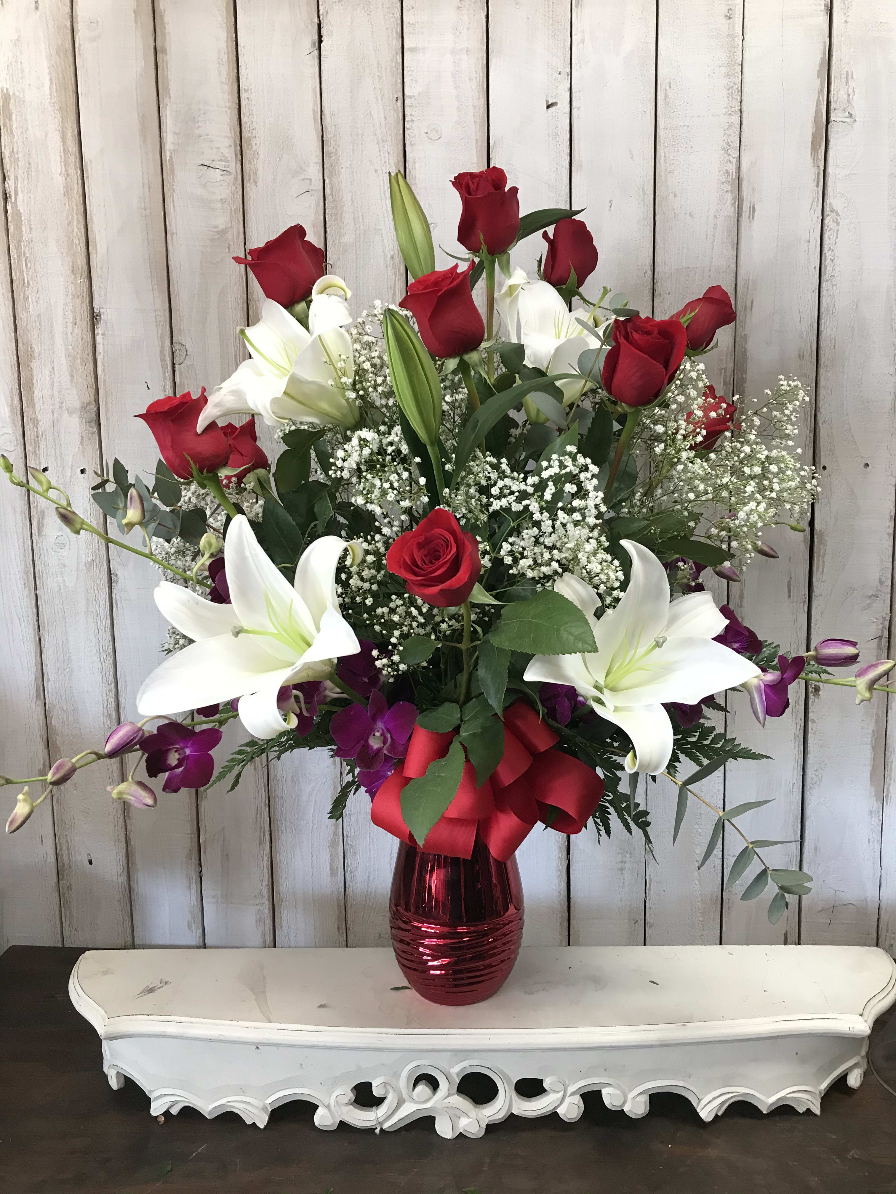 Blooming Love - Say our love is always blooming with this beautiful valentine exclusive by Tommy Austin Florist 1 Dozen red roses, 2 stems of pink stargazer Lily’s and  2 stems of purple orchids, arranged in a red keepsake vase with babies breath and greens. This elegant arrangement is sure to impress. Height 29” this is our valentine special will supplies last only 