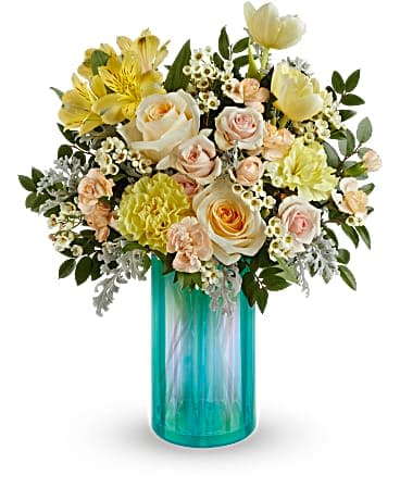 Teleflora's Lovely Luster Bouquet - Capture the magic of early spring sunshine with this bouquet of golden blooms in an iridescent, aqua glass vase that shimmers in the light. This bouquet features light yellow roses, peach spray roses, yellow tulips, yellow carnations, miniature peach carnations, white waxflower, huckleberry and silver lace dusty miller. Delivered in an Iridescent Dream Vase.