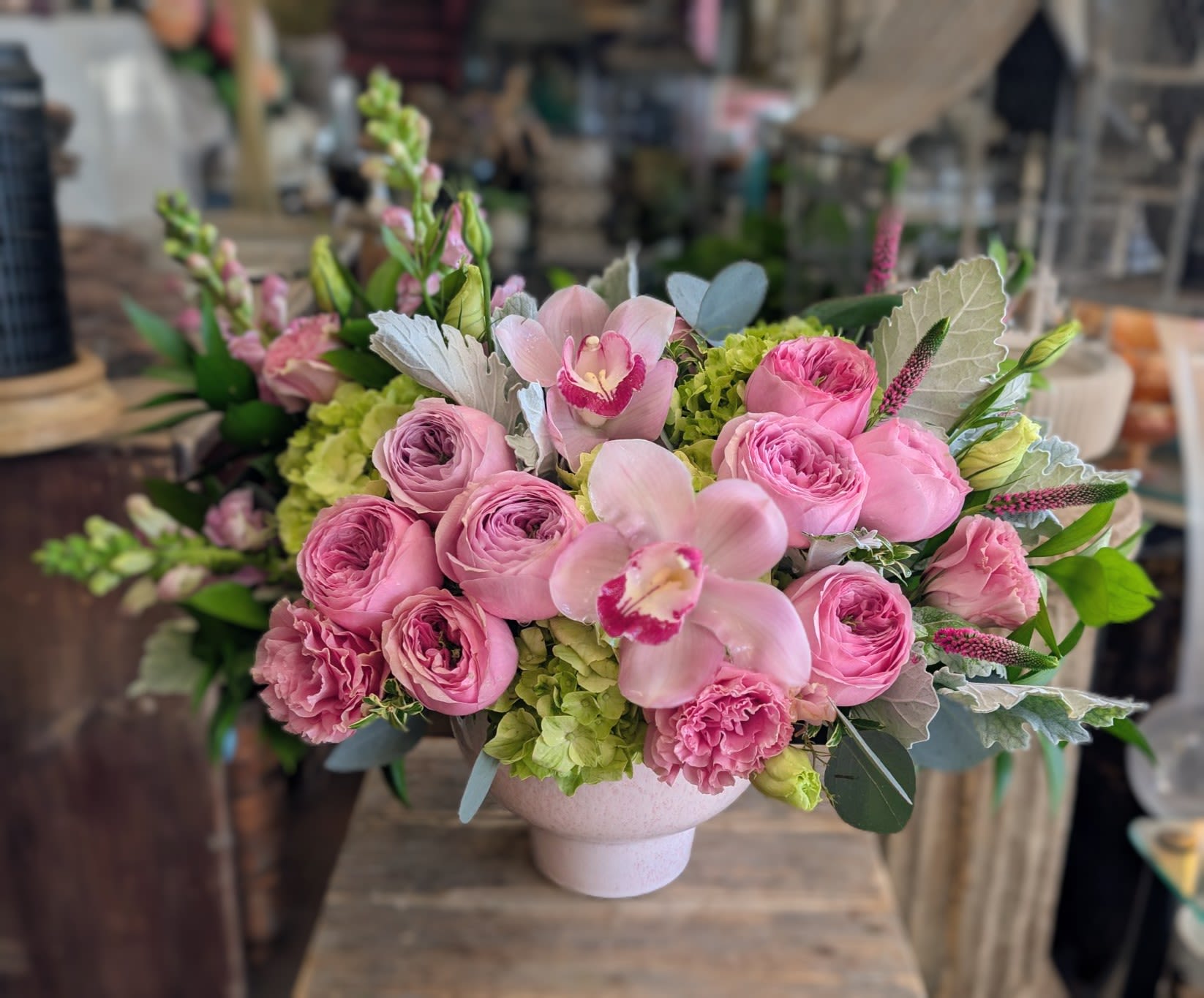 Geneviève - Geneviève is a refined expression of modern floral luxury — an elegant garden-style arrangement designed for those who appreciate timeless beauty and impeccable craftsmanship. Lush pink garden roses unfold in soft layers alongside graceful cymbidium orchids, textural hydrangea, and seasonal premium blooms, all accented with silvery foliage and fresh verdant greens. The palette is romantic yet elevated, striking a perfect balance between softness and sophistication.  Handcrafted by Windmill Floral Expressions in Las Vegas, Geneviève is artfully arranged in a chic ceramic vessel, creating a polished centerpiece suitable for the most discerning spaces. Each bloom is thoughtfully placed to evoke movement and depth, offering a European-inspired design that feels both classic and contemporary.  Ideal for Valentine’s Day, anniversaries, celebrations, or elevated everyday gifting, Geneviève is perfect for clients seeking luxury flower delivery in Las Vegas and Henderson. This arrangement brings understated glamour to dining tables, entryways, offices, and special moments, making it a beautiful statement of love, gratitude, or refinement.  Whether you’re searching for a romantic floral arrangement, luxury roses, or a signature design from a premier Las Vegas florist, Geneviève delivers timeless elegance with effortless grace.