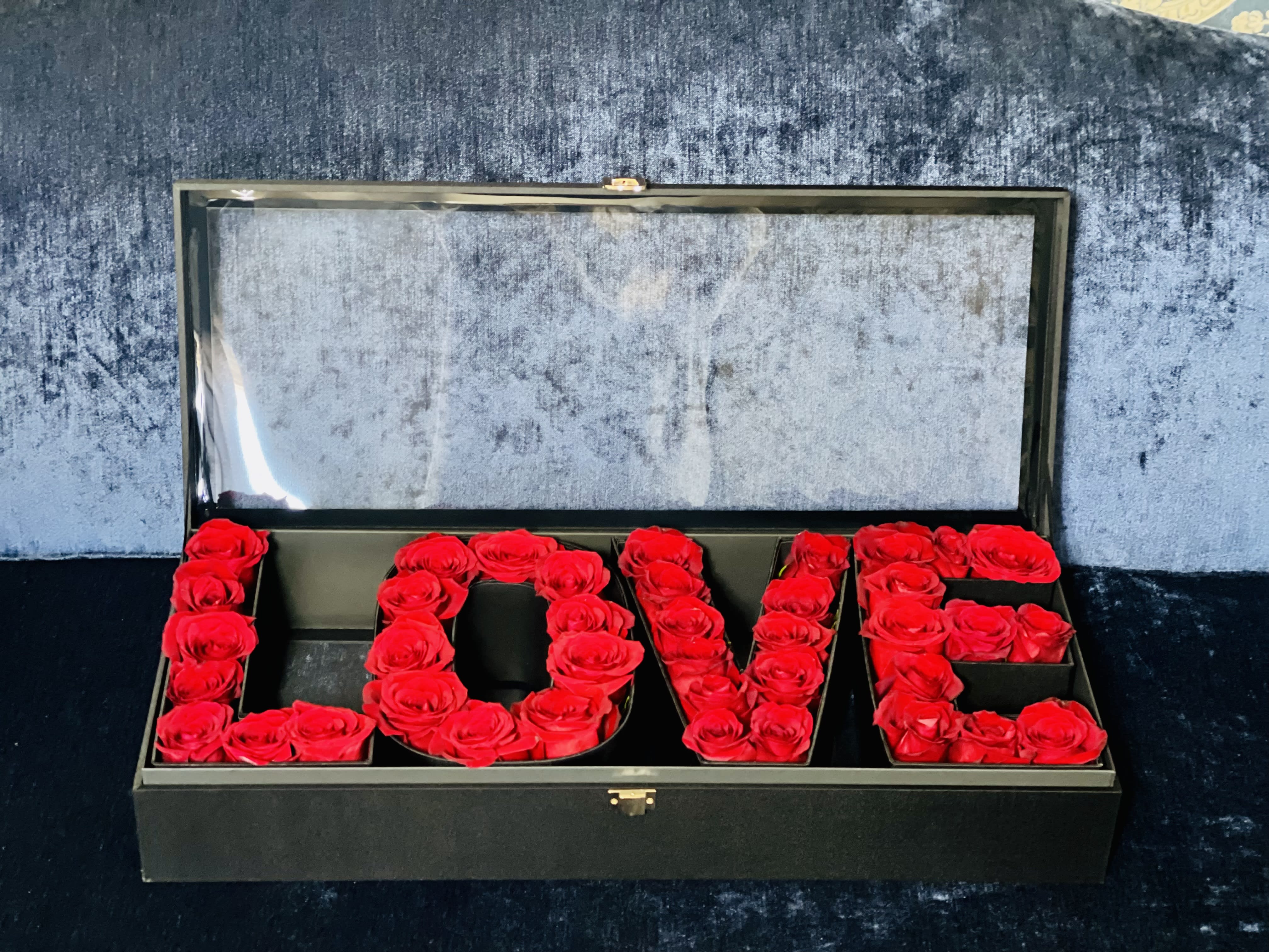  In Love with You  by Flower Carriage - Above and beyond is always the right move! This show-stopping "LOVE" box is the peak of luxury. This arrangement includes about 40 red roses in a grand suitcase box. This box serves perfectly as a dining room centerpiece or in the entryway of your home, pulling together any room with beauty. Roses colors Red, Pink, White, Black, Purple, Silver, Gold,Orange,   Approx. dimensions: W: 26" x 10 1/2" H: 5"   Around 35-40 roses *Customize to any color roses  (If you would like to change the box color or rose color please leave it in the notes or call us, if not it will be ordered as pictured) 