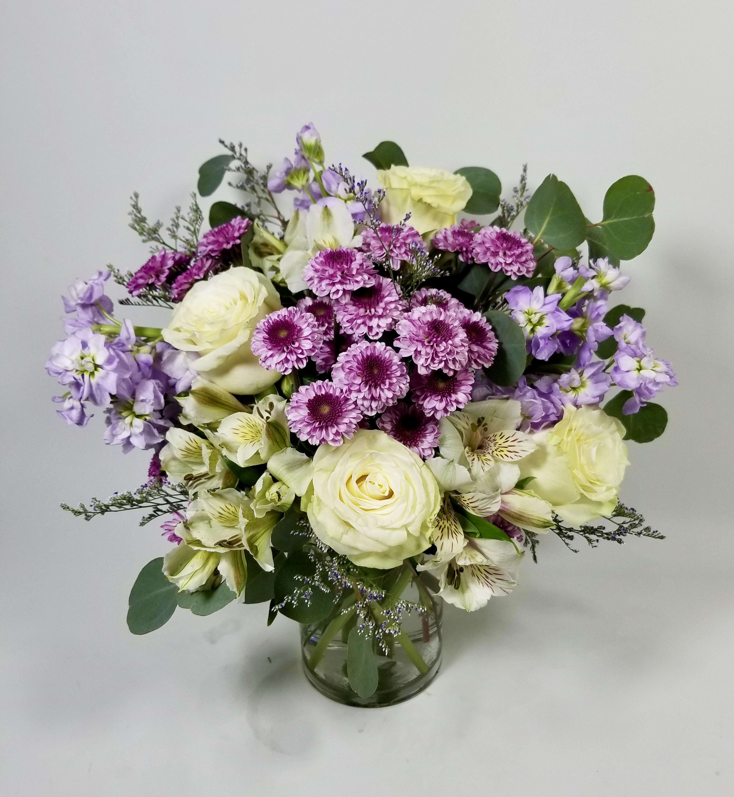 Lavender, Pink and White Expressions - Beautiful French style bouquet floral arrangement created with the best quality flowers. White roses, lavender stock, white alstroemerias, floral fillers, and greenery in a clear vase keeping a loose design. 