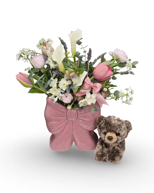 Bow-licious Bundle - Bow-licious is a charming arrangement filled with soft, pastel blooms designed in a keepsake bow-shaped ceramic vase and paired with a sweet little plush bear. Playful and full of heart, this gift blends fresh flowers with a cuddly keepsake for an extra-special surprise.  Includes: -Bow-licious arrangement -Brownie Bear
