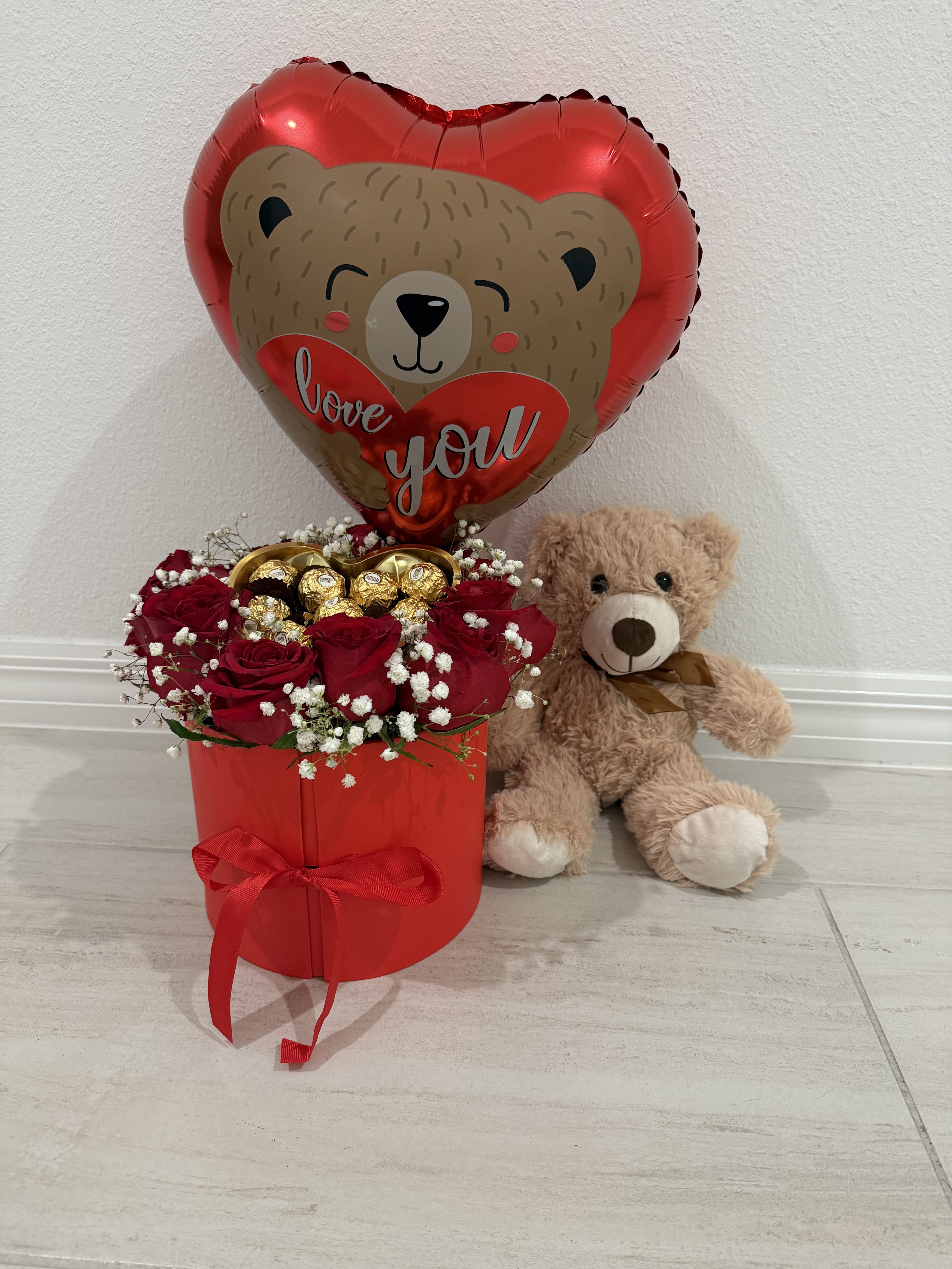 	Amour Luxe Surprise Box - An elegant red round surprise box that opens to reveal space for an additional gift, filled with fresh red roses and delicate baby’s breath. The arrangement features premium Ferrero Rocher chocolates, a heart-shaped “Love You” teddy bear balloon, and a soft plush teddy bear with a satin ribbon. Designed to create a heartfelt and unforgettable romantic surprise. 
