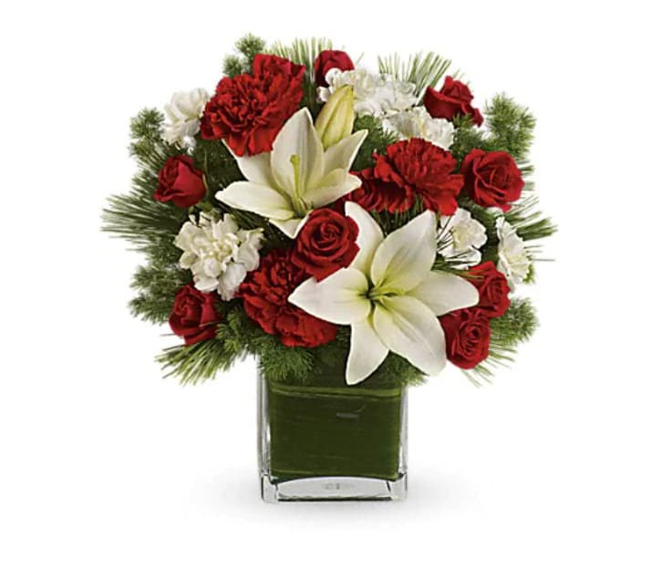 Enchanted Winter Bouquet - It's a Christmas classic! Featuring fragrant lilies, ravishing roses and fresh pines, this stunning snow white and crimson bouquet delivers your heartfelt holiday wishes. Beautiful white asiatic lilies and mini carnations are mixed with luxurious red roses and large red carnations. Winter greens include white pine, noble fir and ming fern. Delivered in a sophisticated clear cube vase lined with a green ti leaf.   Orientation : One-Sided  All prices in USD ($)  Standard  T596-9A