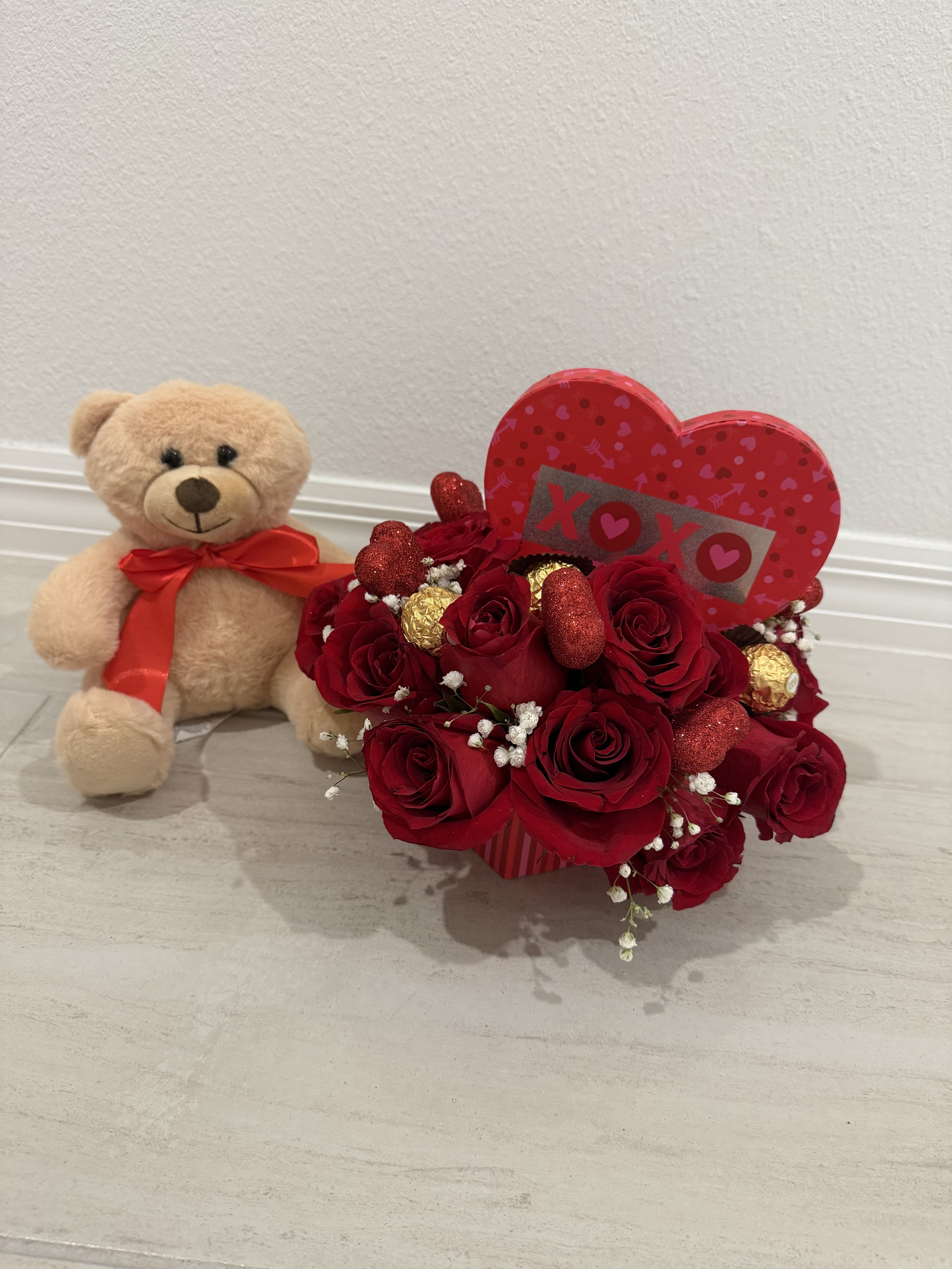 XOXO Teddy Rose Box - Send hugs and kisses with this sweet and romantic floral gift. This arrangement features fresh red roses accented with delicate baby’s breath and premium Ferrero Rocher chocolates, beautifully designed in a red decorative box. Finished with a charming “XOXO” heart topper and paired with a soft plush teddy bear with a satin bow, this arrangement is perfect for Valentine’s Day, anniversaries, or any moment when love deserves to be celebrated