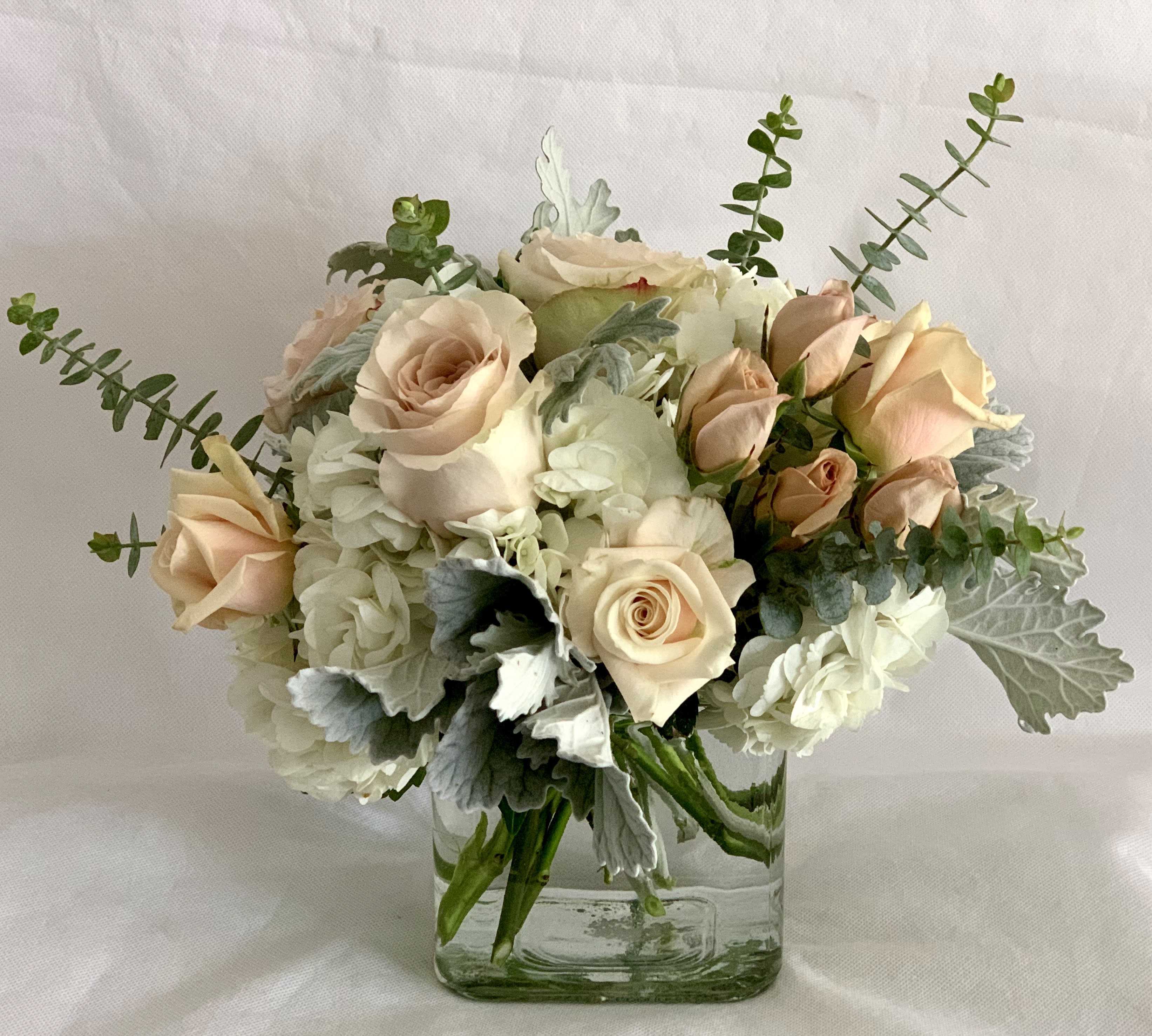 Sahara elegance - An elegant blend of soft blushes, white and dusty greenery in a clear glass vase. The deluxe version includes more blooms than the standard version and is in a bigger container. The premium version is a large and spectacular version of this arrangement, featuring seasonal premium blooms.