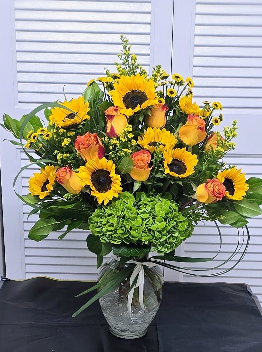Golden Sunflower Celebration - A bold and radiant arrangement featuring cheerful sunflowers, vibrant orange-yellow roses, and a lush base of green hydrangea. Designed tall with fresh greenery and golden filler blooms, this bouquet is perfect for celebrating life’s biggest moments and bringing warmth and happiness into any space.