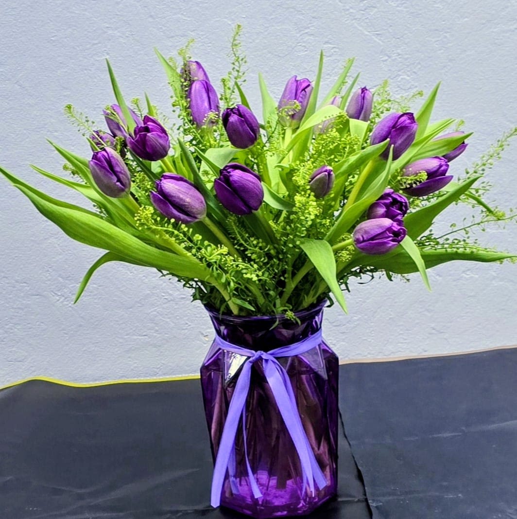 Purple Tulip Charm - A sleek and stylish arrangement of rich purple tulips paired with fresh green foliage, designed in a matching purple vase for a bold monochromatic look. Simple, modern, and elegant — perfect for springtime gifting or anyone who loves clean, sophisticated floral design.
