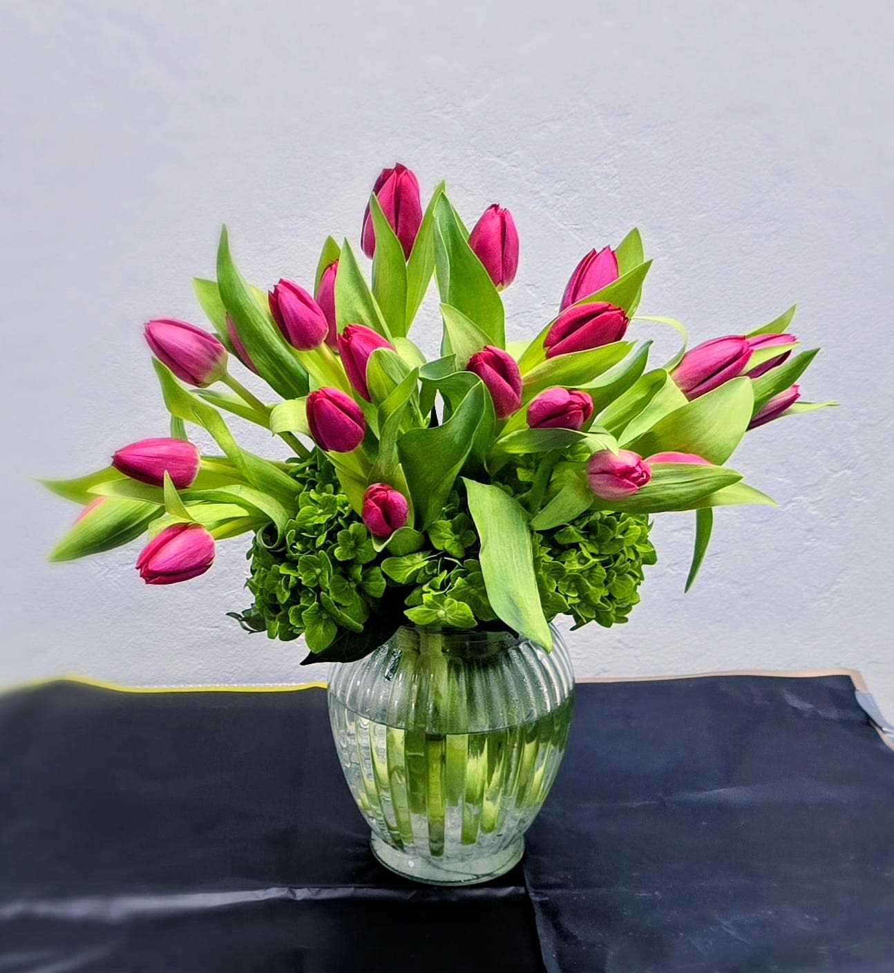 Pink Tulip Freshness - A vibrant and modern arrangement featuring bold pink tulips nestled above lush green hydrangeas. Designed in a clear glass vase, this bouquet is the perfect springtime gift — bright, fresh, and full of life. Simple, elegant, and guaranteed to make someone smile.