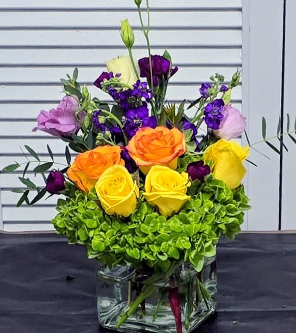 Citrus Garden Pop - A cheerful modern arrangement featuring sunny yellow and orange roses nestled into a lush green hydrangea base, accented with vibrant purple blooms. Compact, colorful, and full of personality, this bouquet is perfect for brightening someone’s day with a fresh pop of color.