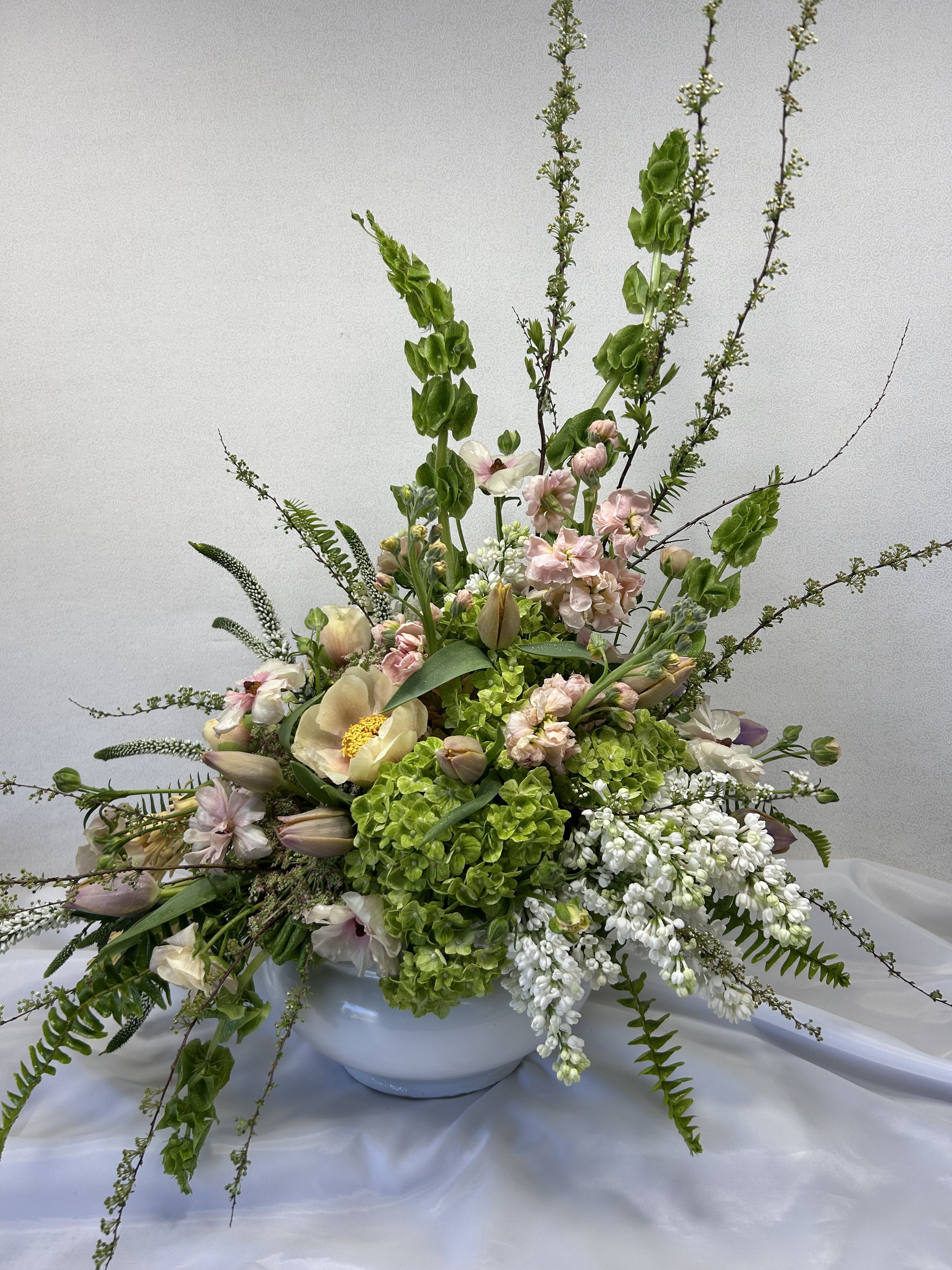 Belles of Europe - This elegant floral arrangement is a wonderful focal point for any special event. Ceramic container with Belles of Ireland, Ranunculus, Peonies, Tulips, Stock and accent flowers. Tulips will be used if in season. We will use a suitable replacement of the same value when not in season.