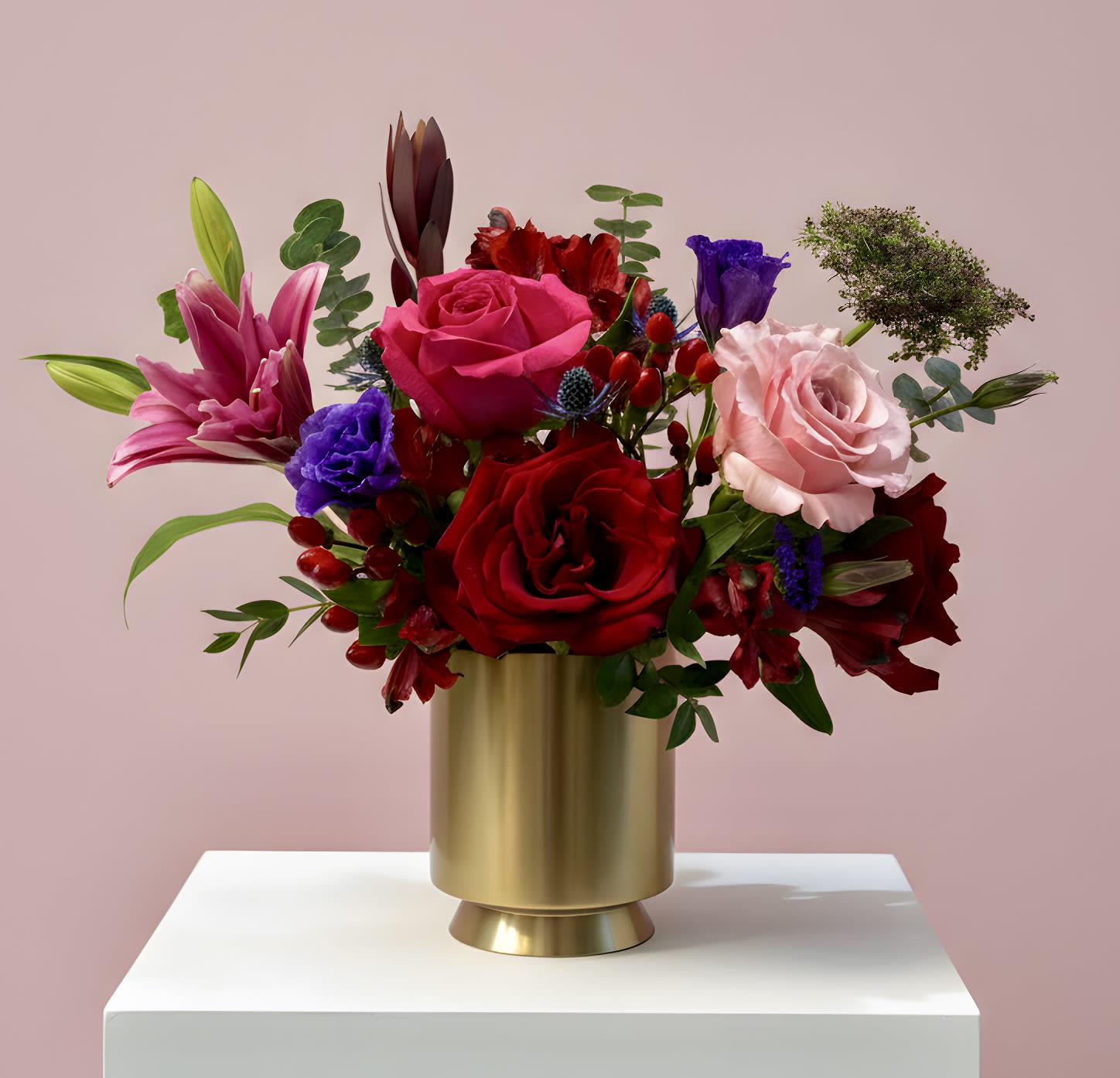 Ruby &amp; Blush - A captivating arrangement of red, hot pink, and soft blush blooms accented with touches of purple, artfully designed in a gold vase. Romantic, vibrant, and full of depth, this piece is made to turn heads and celebrate life’s most meaningful moments—perfect for any occasion.