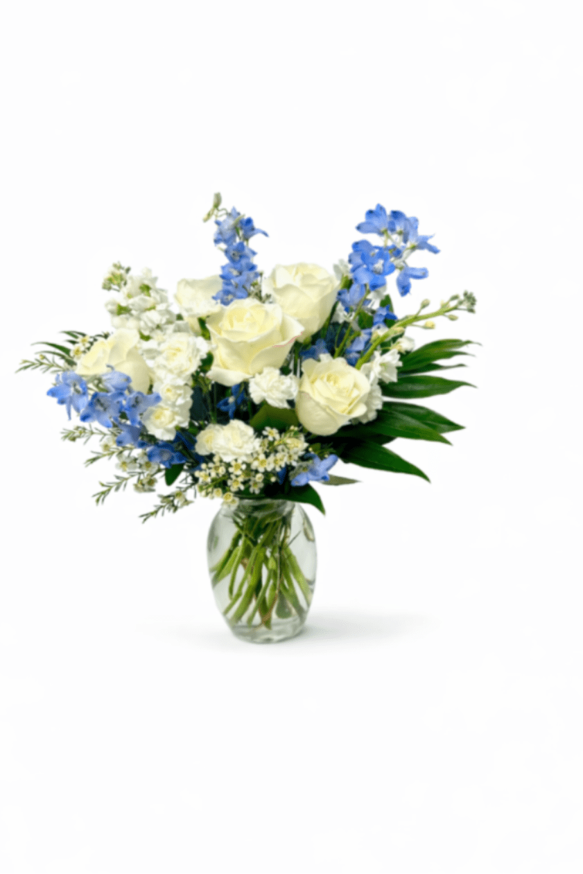 Elegant Blue &amp; Ivory Garden Bouquet - A refined hand-designed bouquet featuring premium ivory roses accented with soft blue delphinium, white carnations, delicate waxflower, and lush seasonal greenery. Arranged in a clear glass vase, this design blends freshness, elegance, and natural movement, making it a timeless floral gift for any meaningful occasion.  Better For: Birthday, Sympathy, Thank You, Get Well, Thinking of You, New Baby, Home Décor