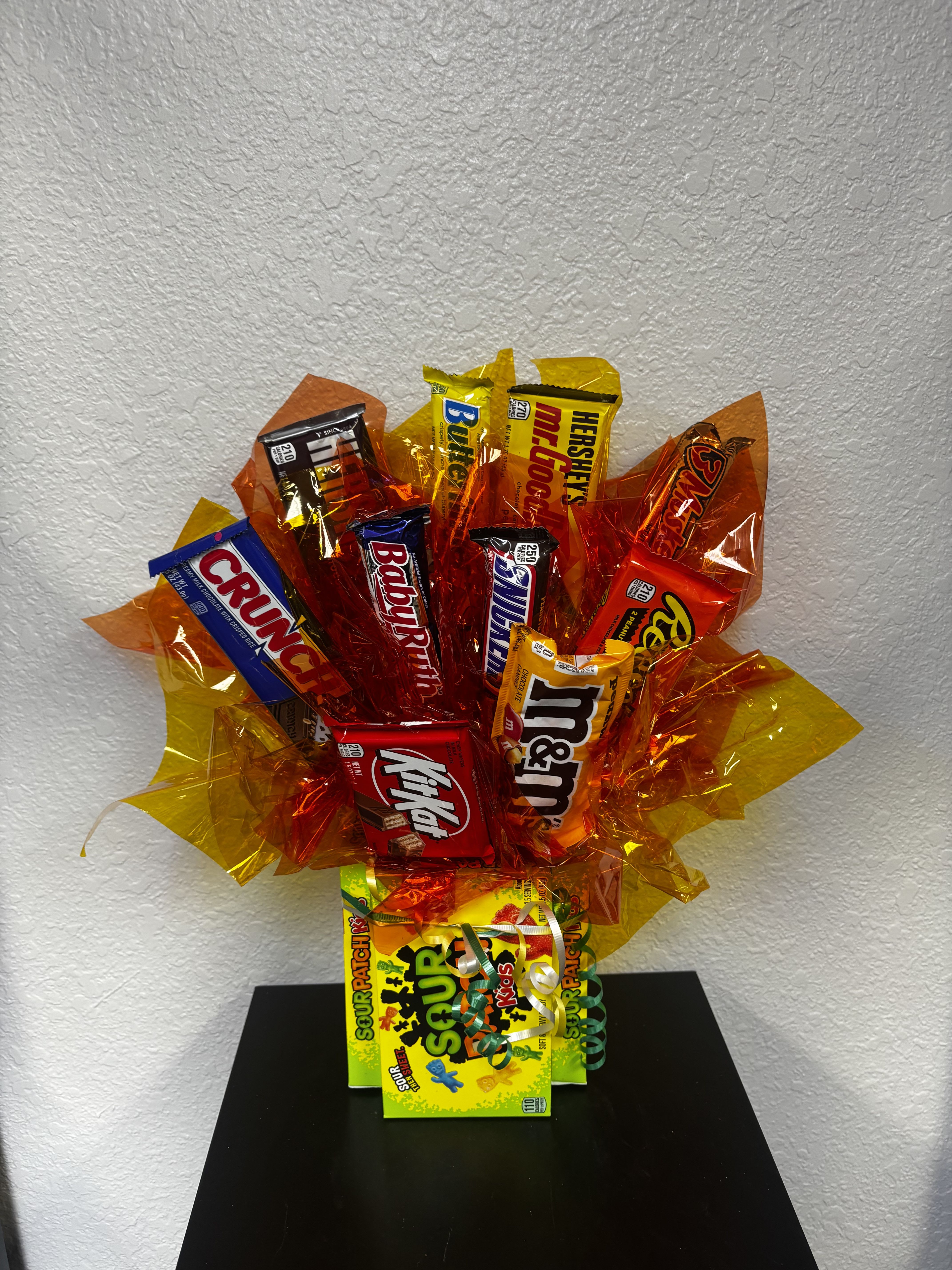 Sour Patch Kids Candy Bouquet  - A candy lover’s dream! This colorful candy bouquet is loaded with a mix of classic chocolate bars and chewy treats, all beautifully arranged in vibrant red, orange, and yellow wrap for a festive “burst” look. Finished off with a fun Sour Patch Kids base, it’s the perfect grab-and-go gift for birthdays, thank-yous, get well wishes, or just because.