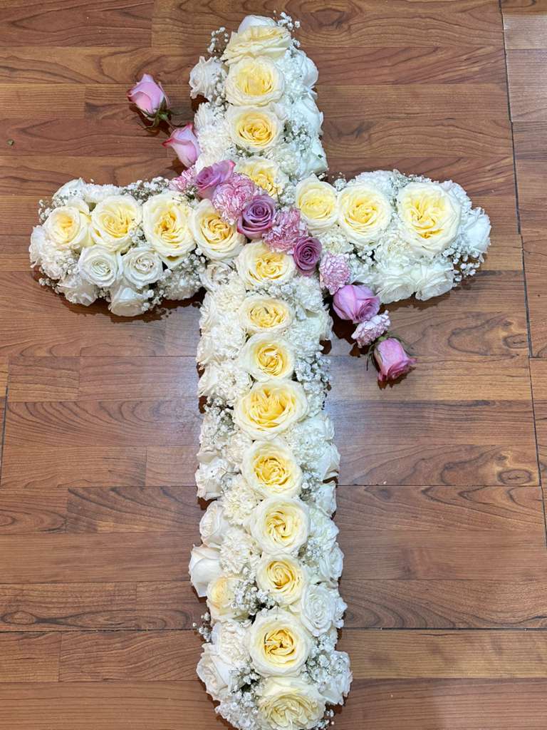 Rest in Harmony - Large cross - A graceful standing cross adorned with fresh white roses and a soft purple floral accent at the center, symbolizing peace, honor, and remembrance. Designed to express heartfelt sympathy and eternal love. Floral colors may be customized according to the client’s preference.