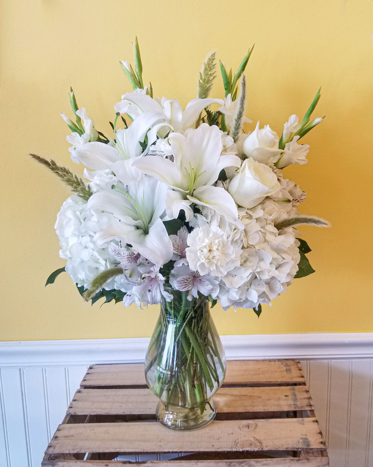 Loving Memory - Send a beautiful arrangement as a symbol of your heartfelt compassion. Elegant from every vantage point, this extraordinary bouquet emphasizes the beauty of  hydrangea, lilies, roses and other white flowers. This is an all white arrangement in a Bella clear vase.  Appropriate for a service or for home arrangement.  *** Arrangement is one sided***