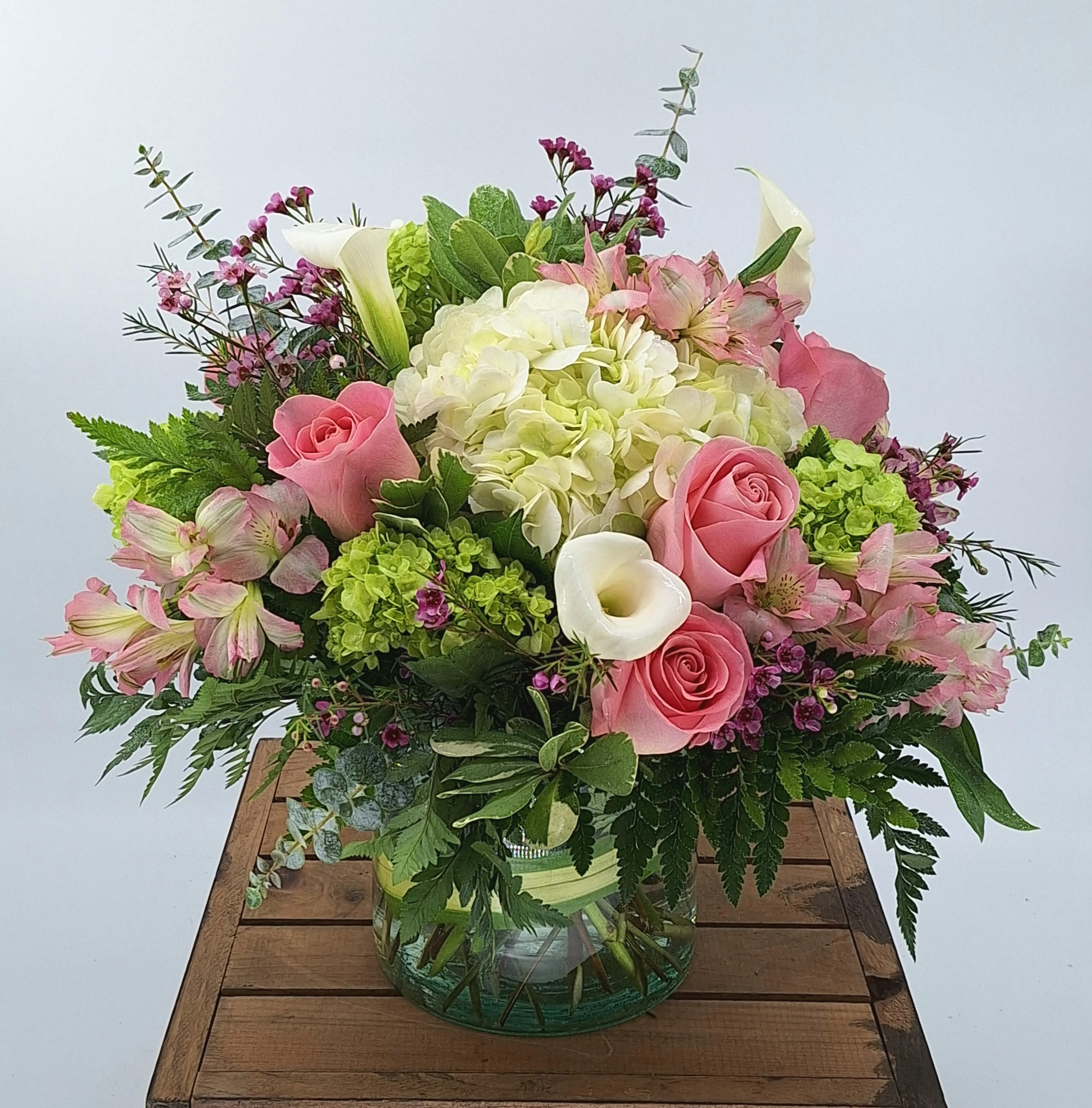 Warm thoughts (DL) - Elevate your space with our modern floral arrangement, a true testament to contemporary elegance. Featuring delicate blush pink roses, vibrant green hydrangeas, mini calla lilies, and more, this arrangement is a captivating blend of sophistication and style. Each stem is expertly curated and skillfully arranged in a leaf-lined glass cylinder vase