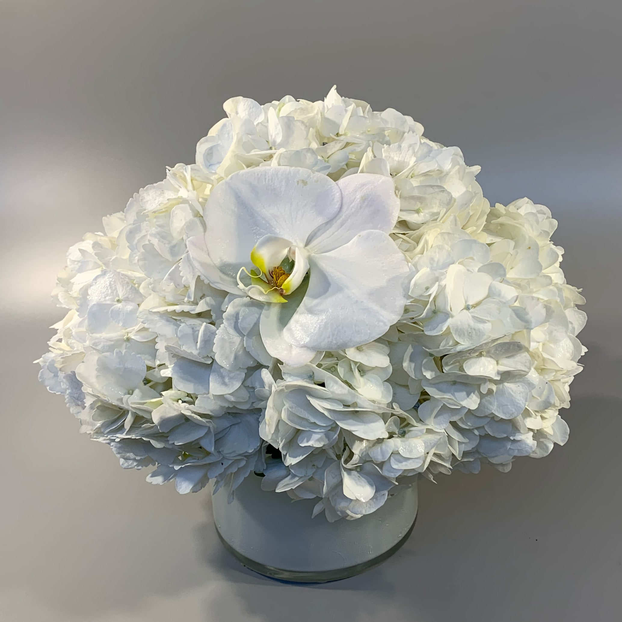 CLOUD - A lush and simple vase designed with a cloud of white hydrangea hand-tied in a white glass cylinder vessel. 