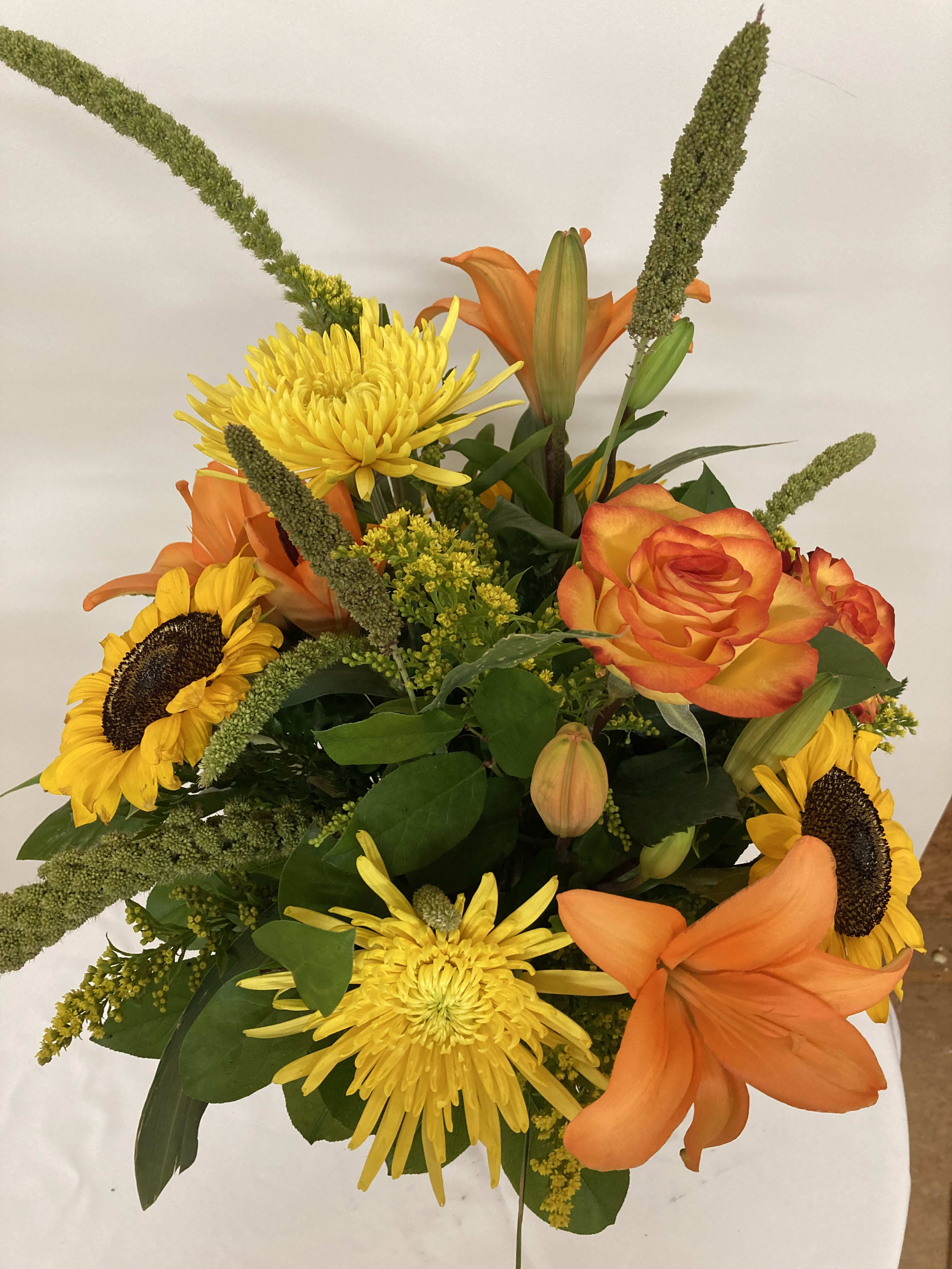 Tropical Delight - Orange  lilies and roses with yellow sunfowers and spider mums surrounded by solidago and acacia greenery.