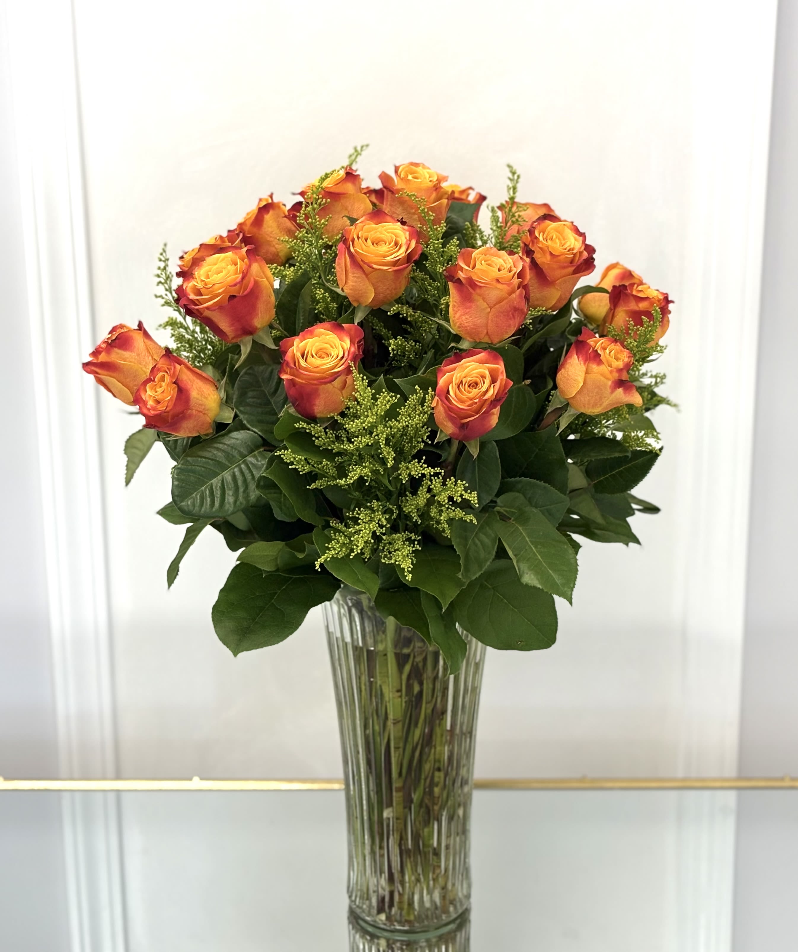 Sunset Glow By VLM Flowers - A radiant bouquet of vibrant orange roses in a classic glass vase—bursting with warmth, energy, and charm, like the golden hour in full bloom. Standard size 12 roses. Deluxe size 24 roses. Premium size 36 roses.