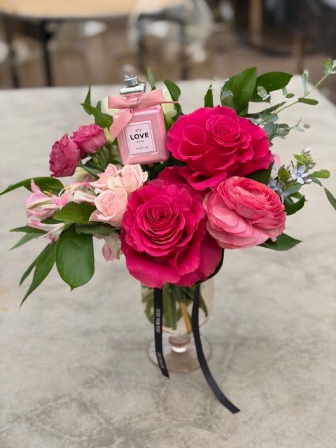 Love Potion - A little flirty, a little magical, and full of romance. Love Potion features vibrant hot pink and blush roses nestled with soft ranunculus, delicate accents, and fresh greenery. Finished with a charming keepsake “Love” perfume bottle, this arrangement is designed to enchant at first glance. Perfect for Valentine’s Day, anniversaries, or anytime you want to cast a spell of love.