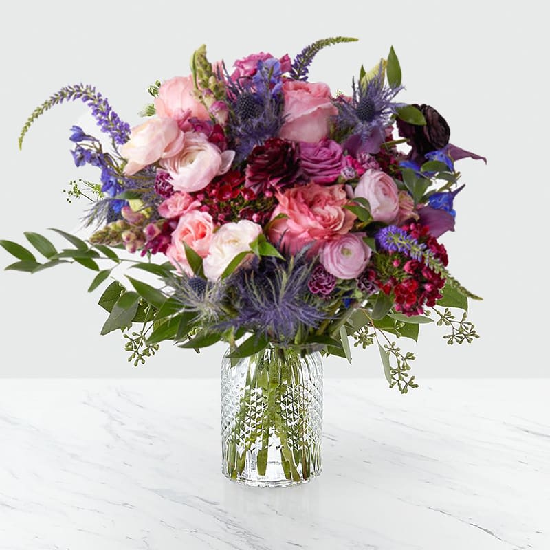 Verona Floral Bouquet - The Verona floral arrangement with Roses, Mini Calla Lilies, Lisianthus, Veronica, Sweet William, Delphinium, and seasonal accents.   Our Verona floral arrangement captures the essence of a secret garden, ideal for enchanting moments or as a sophisticated gift.   Approximately 16" H x 14" W. 