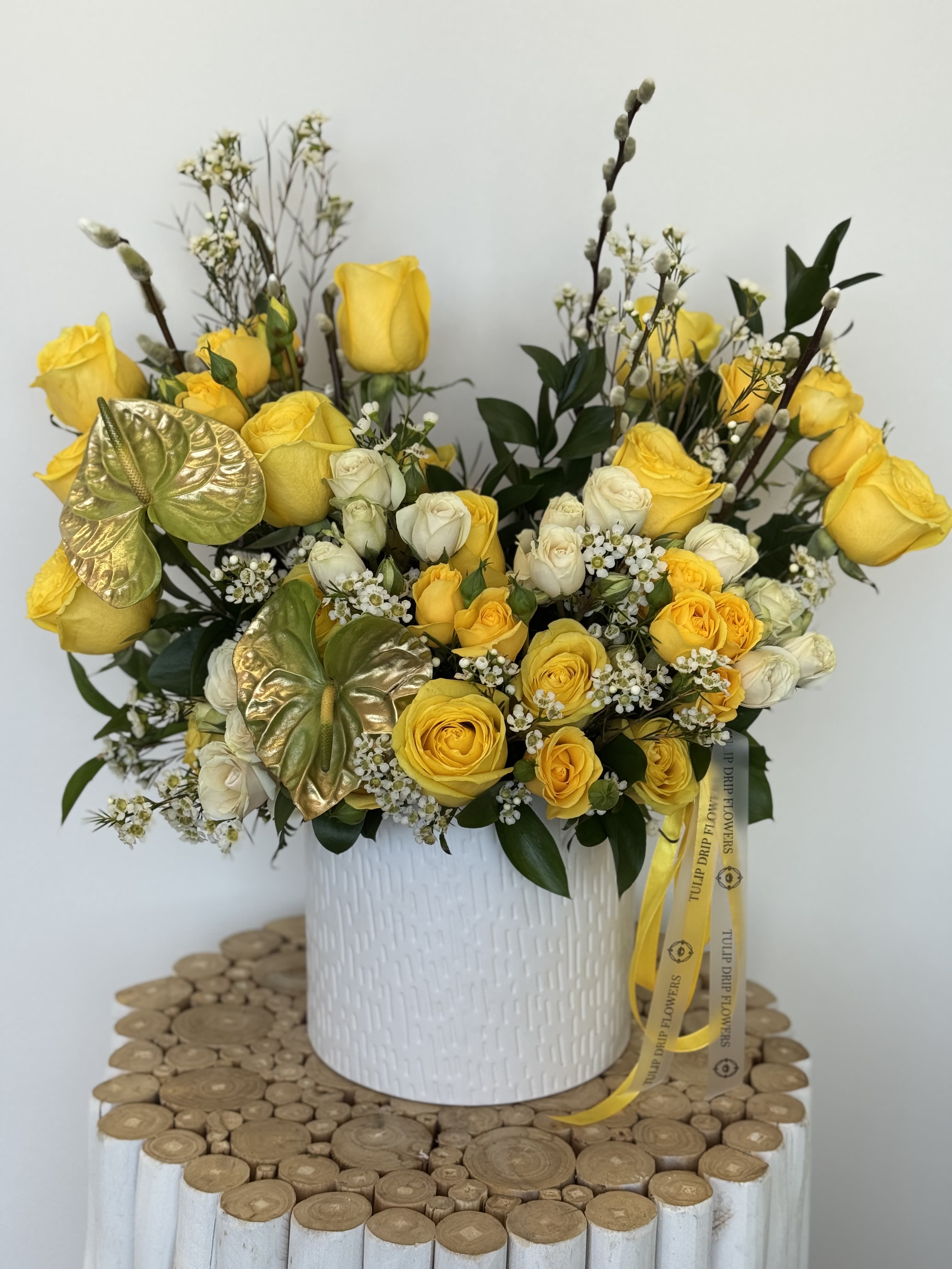 Lemon Rose Charm  - Golden yellow roses, ivory blooms, and white waxflowers arranged in a ceramic white pot with golden anthurium accents. A joyful and radiant choice for celebrating mom.